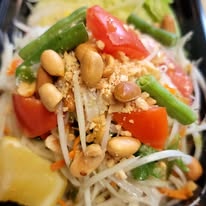 Close-up of a vegetable salad with tomatoes, green beans, bean sprouts, peanuts, and lemon wedge.