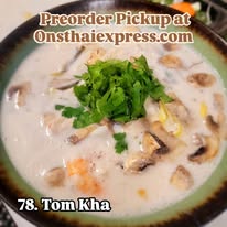 Bowl of Tom Kha soup with green herbs on top, creamy white broth, and pieces of chicken or vegetables, viewed from above.