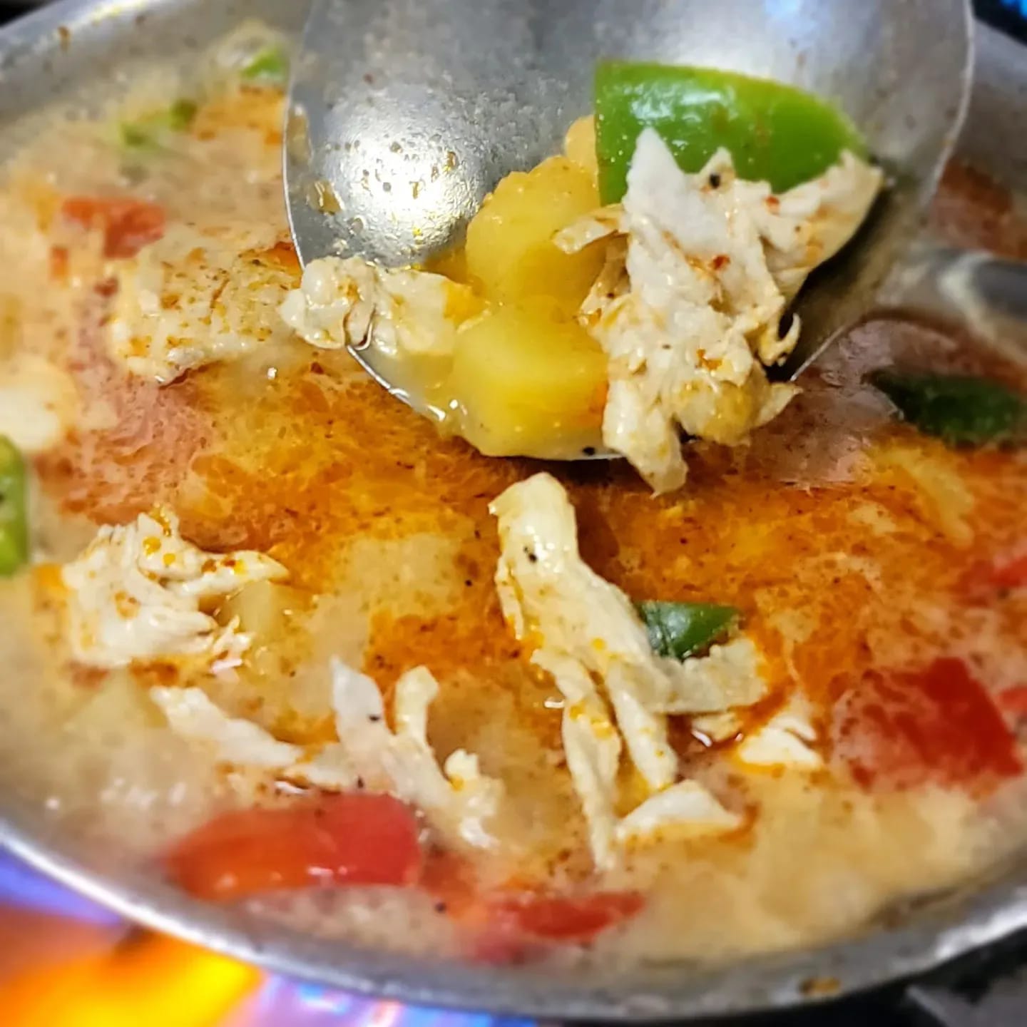Close-up of a spoon scooping chicken, potato, and lime from a bowl of soup with vegetables, in a metal bowl.