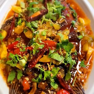 Close-up of a colorful vegetable dish with herbs and spices, garnished with cilantro and chili peppers.