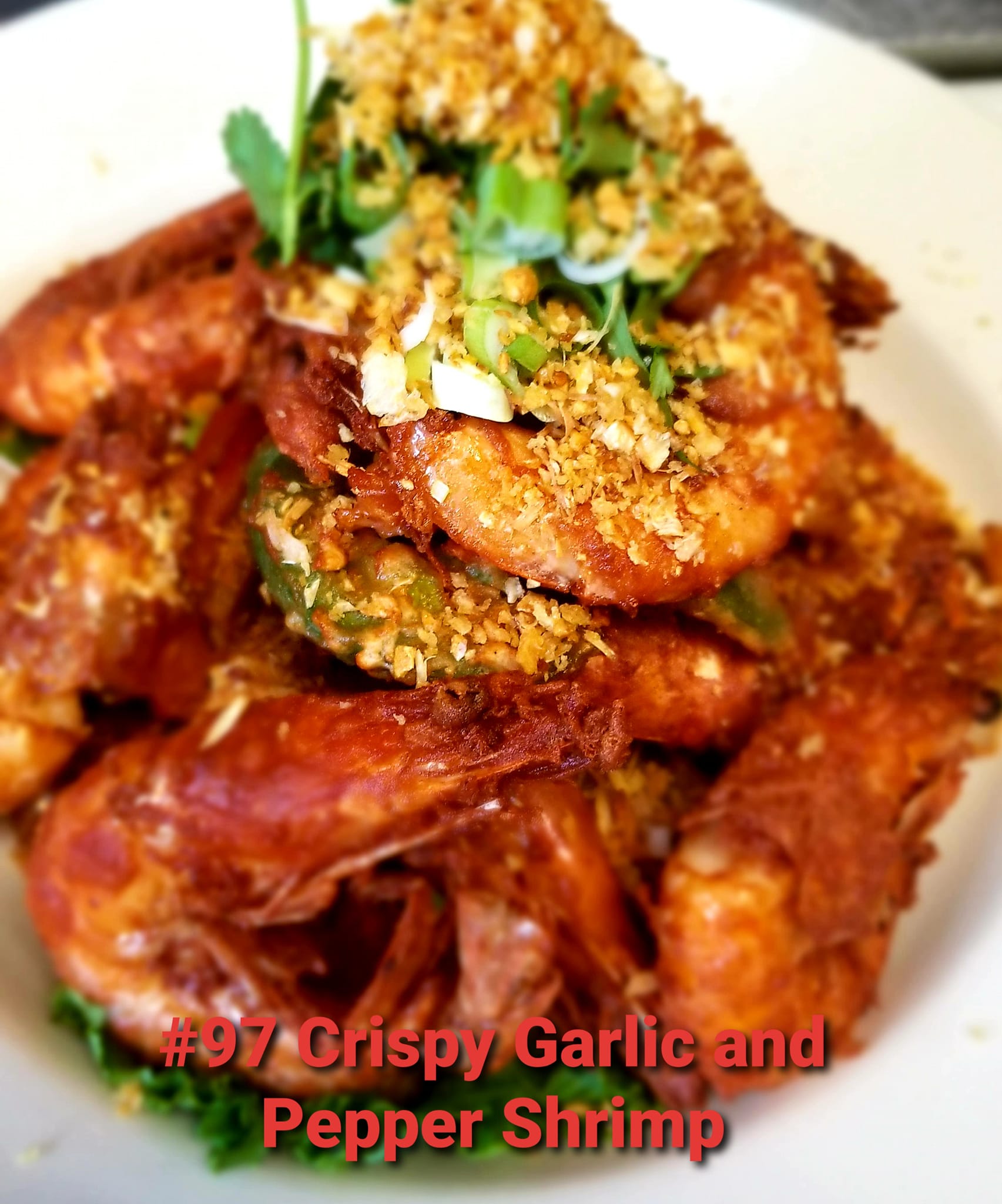 Crispy garlic and pepper shrimp garnished with herbs and crunchy topping on a white plate.