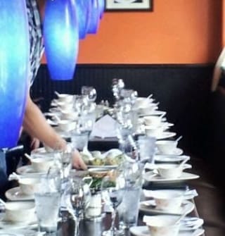 Long table set with glasses, bowls, and plates in a restaurant with orange and black walls.