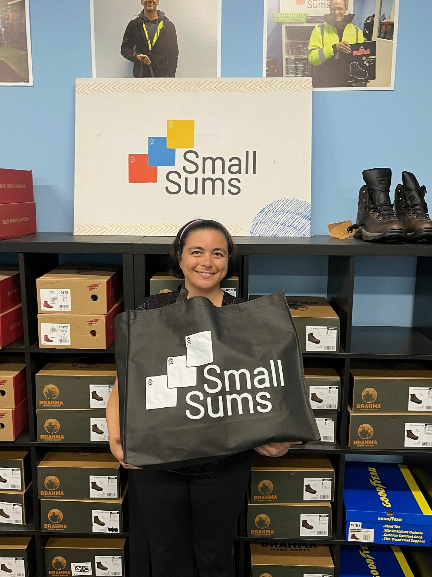 Person holding a large black bag with 'Small Suns' logo, standing in front of shelves with boxes, in an office setting.