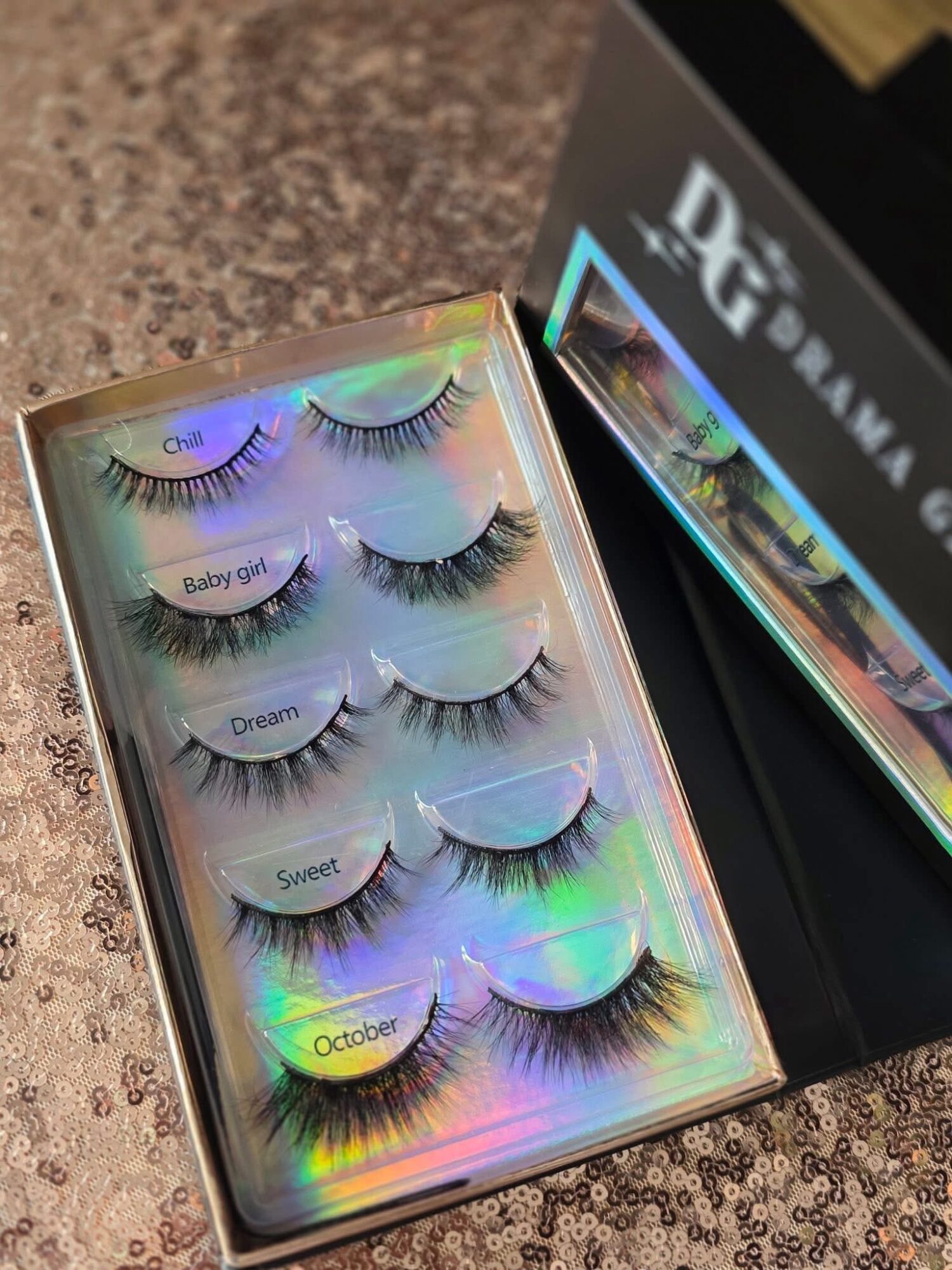 Box of six false eyelashes with labels, colorful holographic background, on a brown surface.