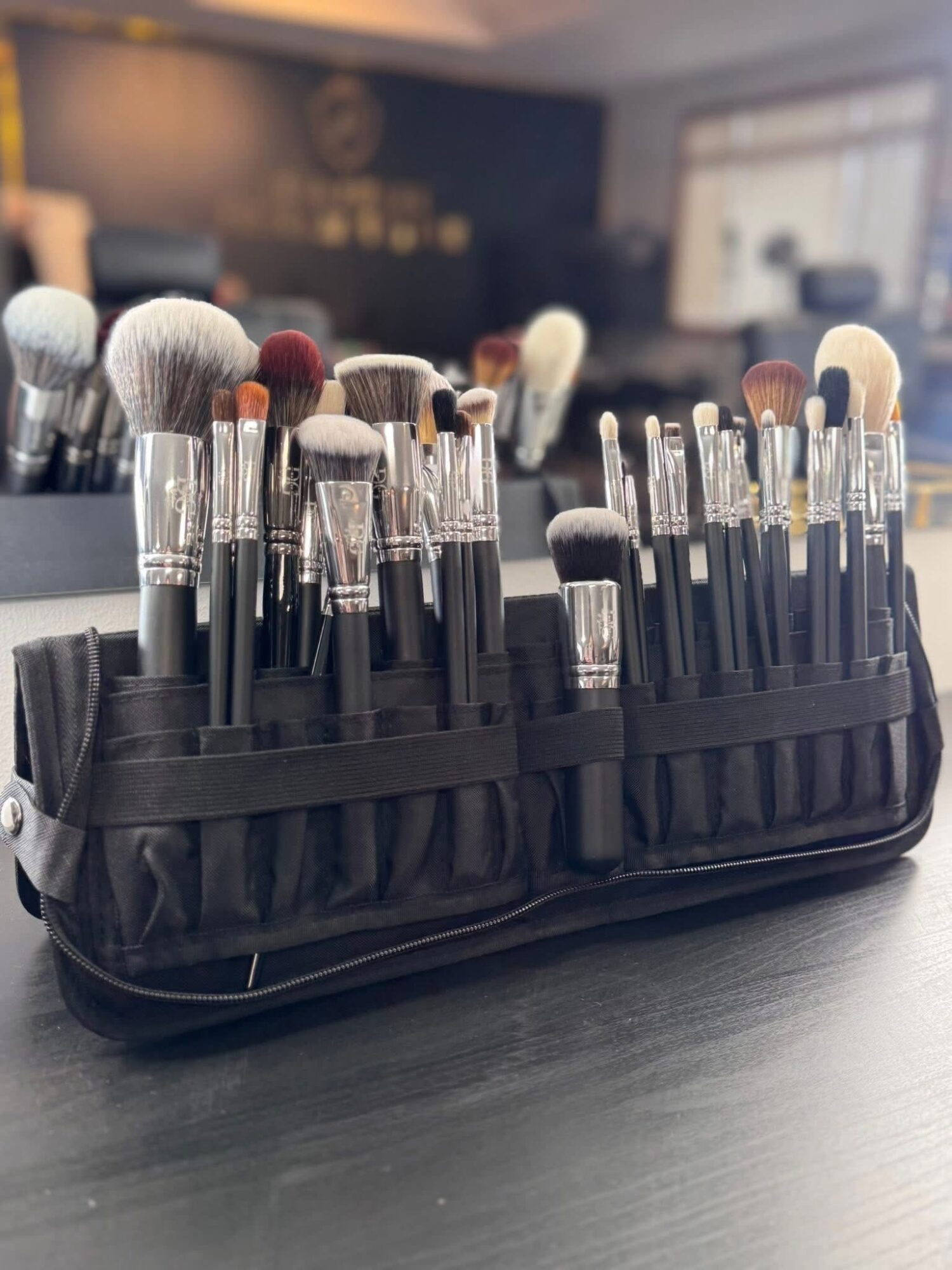 Makeup brushes in a black case on a table, with a blurred background of a room and window.