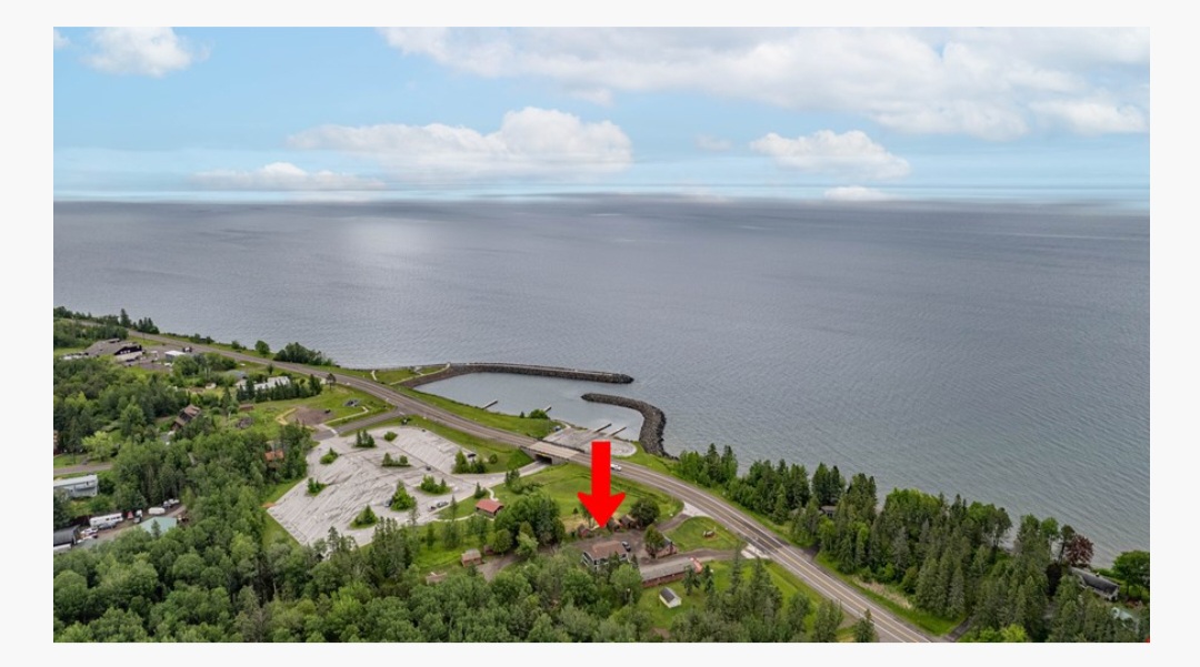 Aerial view of a coastline with a road, trees, and a body of water in the background.