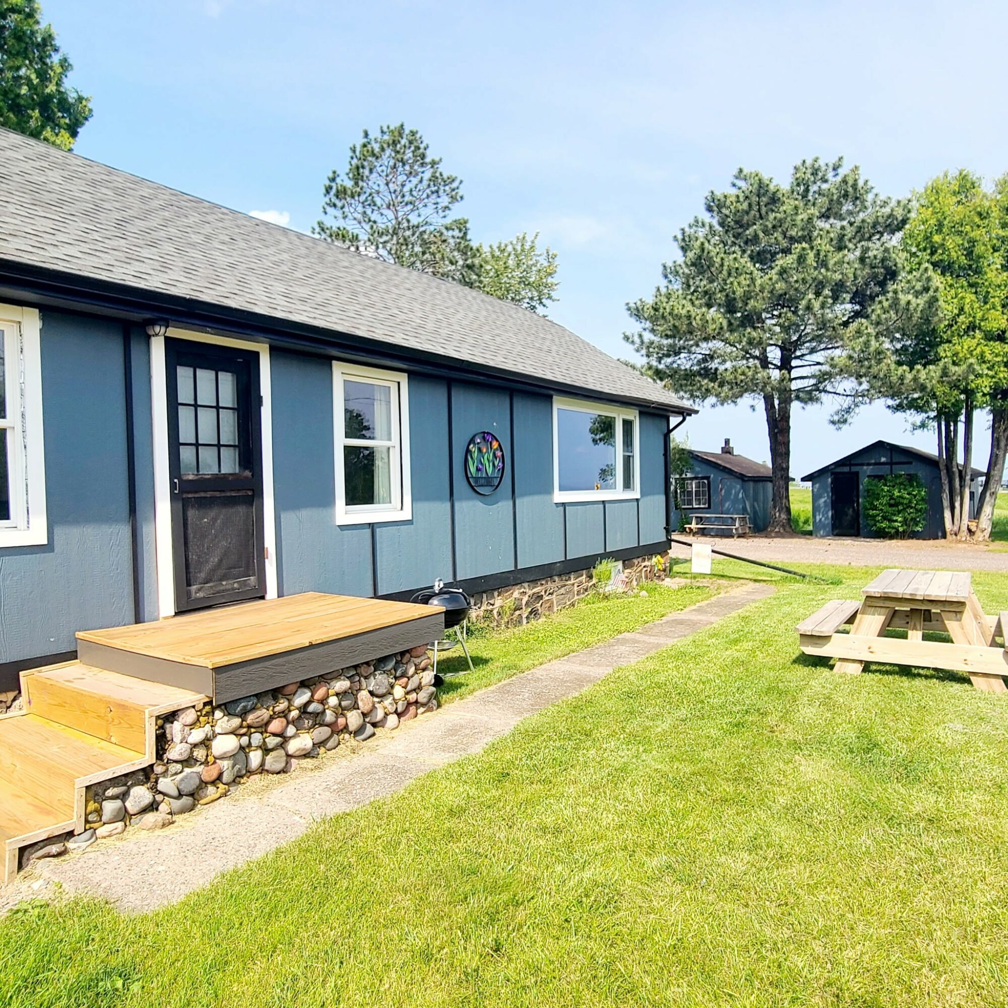 Blue house with white trim, small porch, grassy yard, picnic table, trees, and a clear sky.