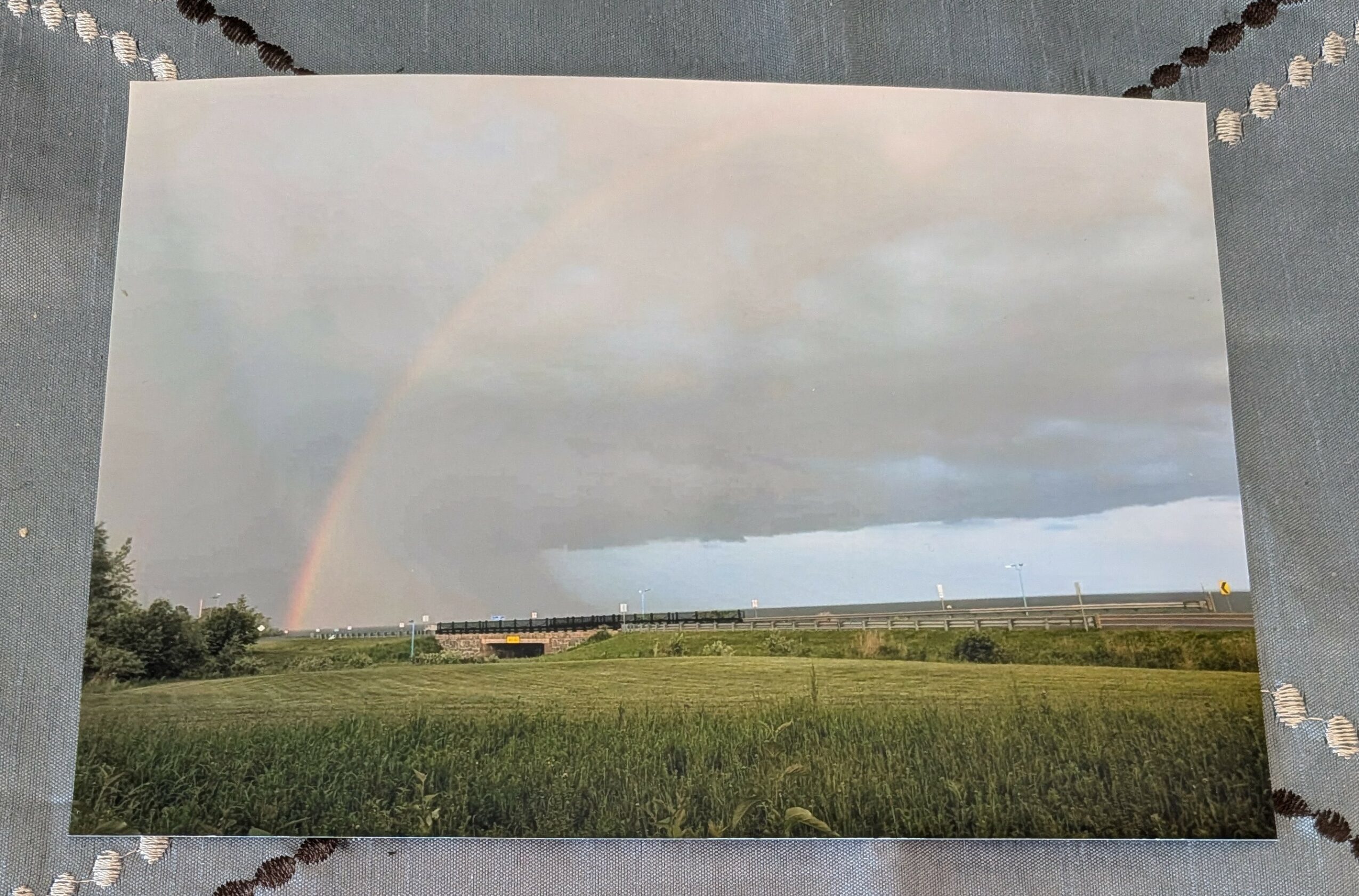Landscape with a rainbow arching over green fields and cloudy sky.