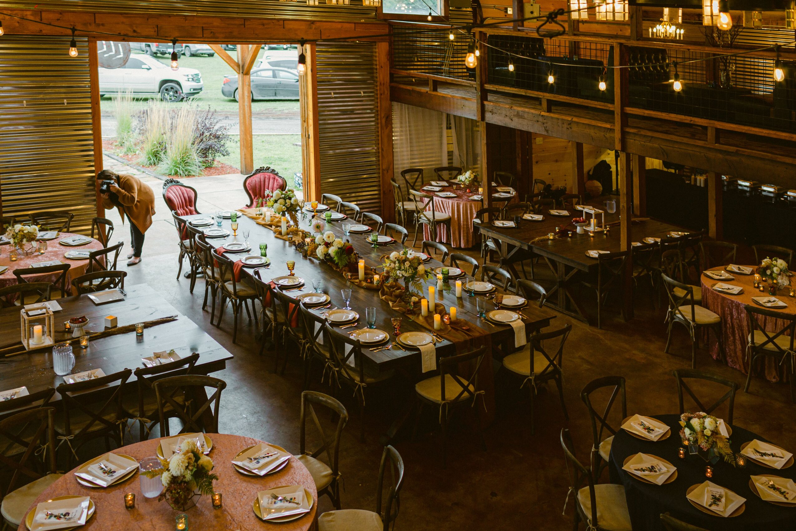 Restaurant interior with a long table set for a meal, surrounded by chairs, with a view outside through large windows.