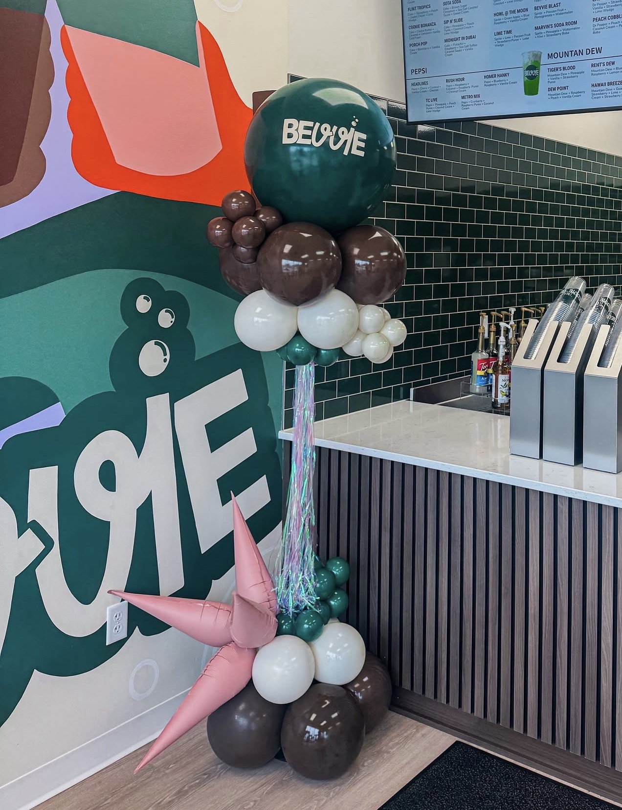 Balloon arrangement with a large teal balloon, pink unicorn balloon, and smaller brown, white, and teal balloons, near a counter.