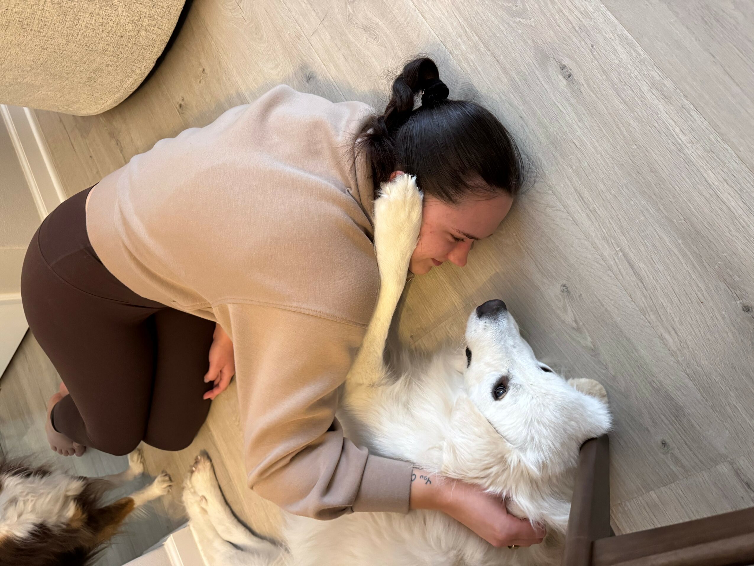 Person lying on the floor with a white dog, both resting their heads on the ground, facing each other.