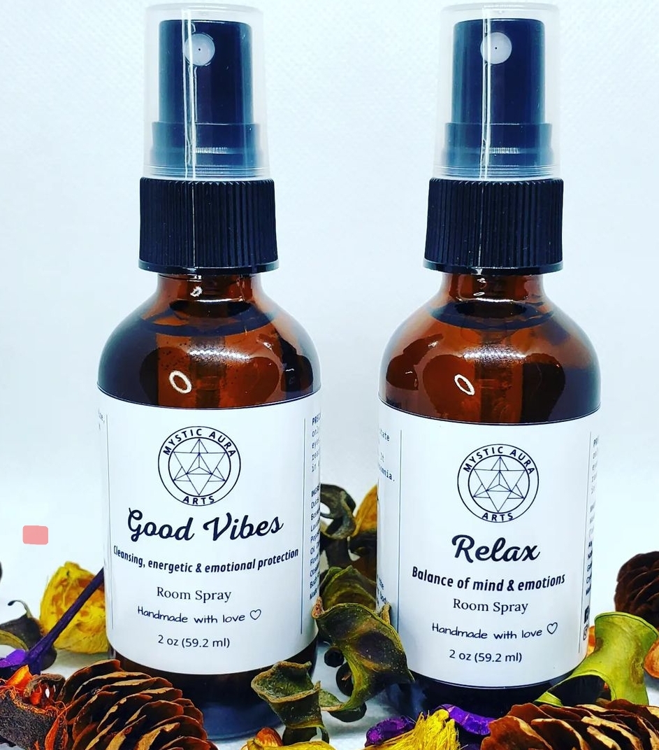 Two amber spray bottles labeled 'Good Vibes' and 'Relax' on a surface with colorful leaves, white background, and black caps.