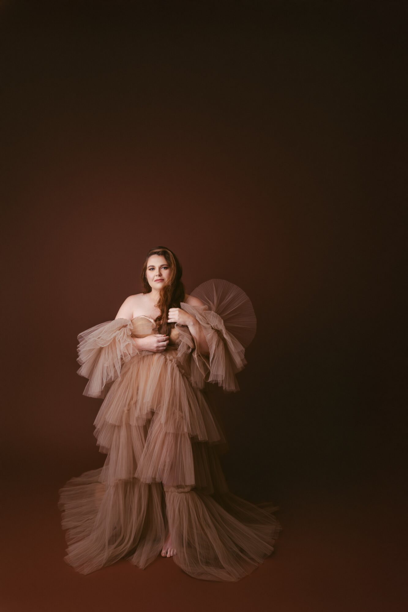Woman in a layered, ruffled gown holding a parasol, standing against a dark background.