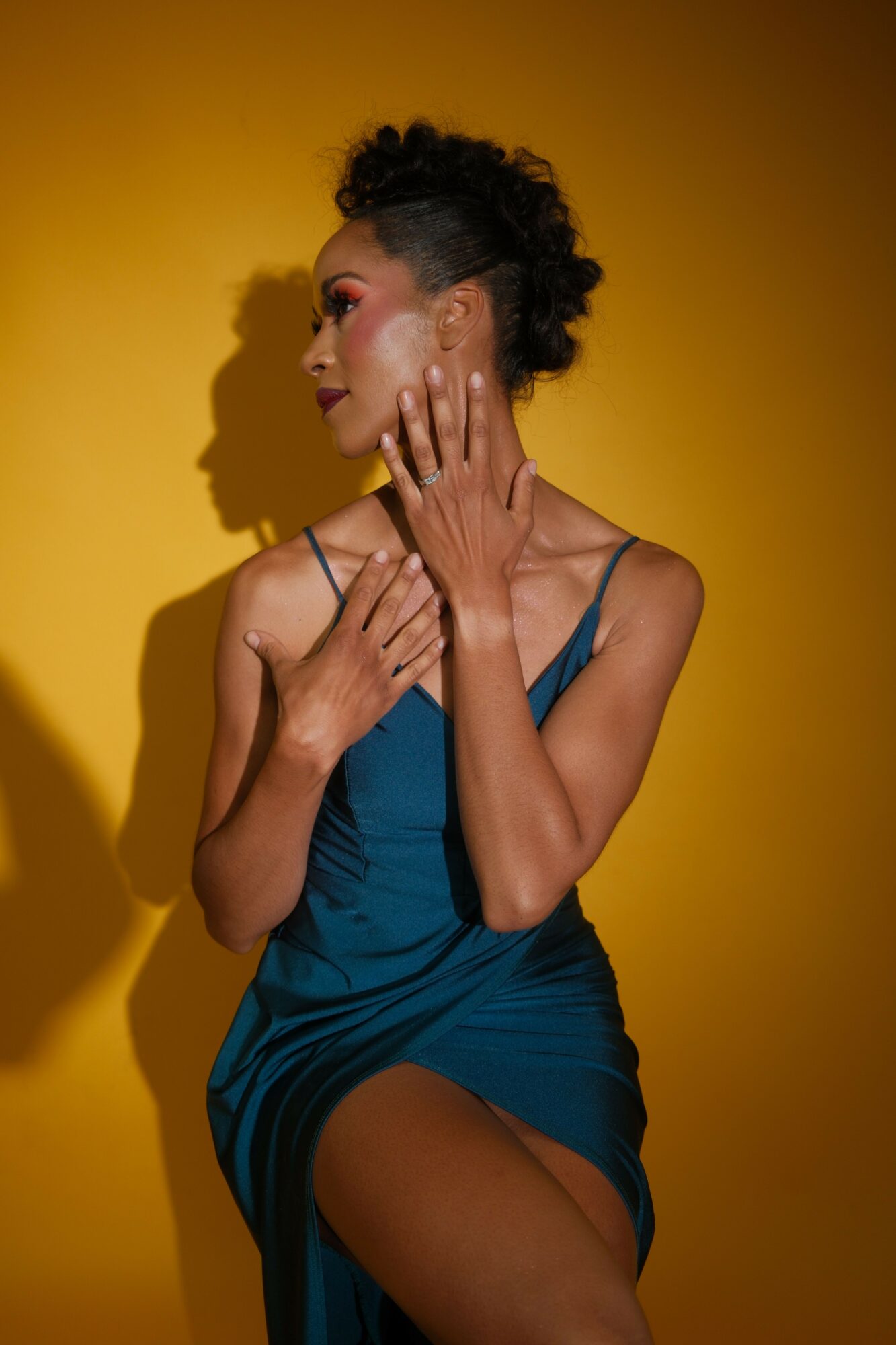Woman in blue dress lying on yellow background, holding her face with hands, eyes closed, expressive face.