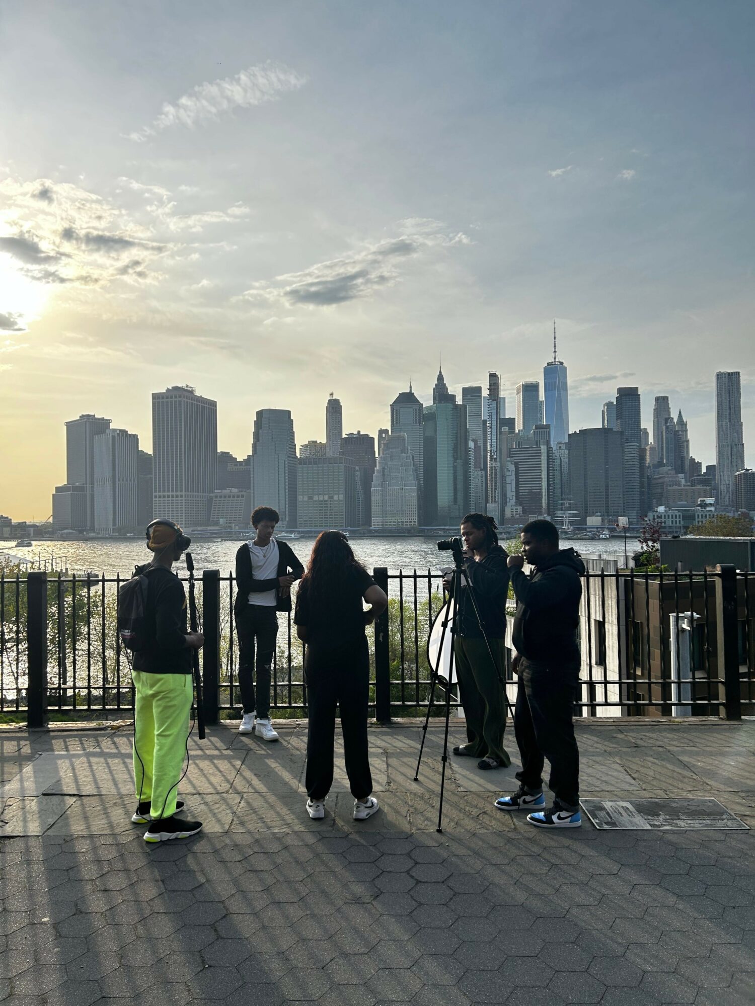 Group of people walking on a paved path with a city skyline in the background, under a cloudy sky.