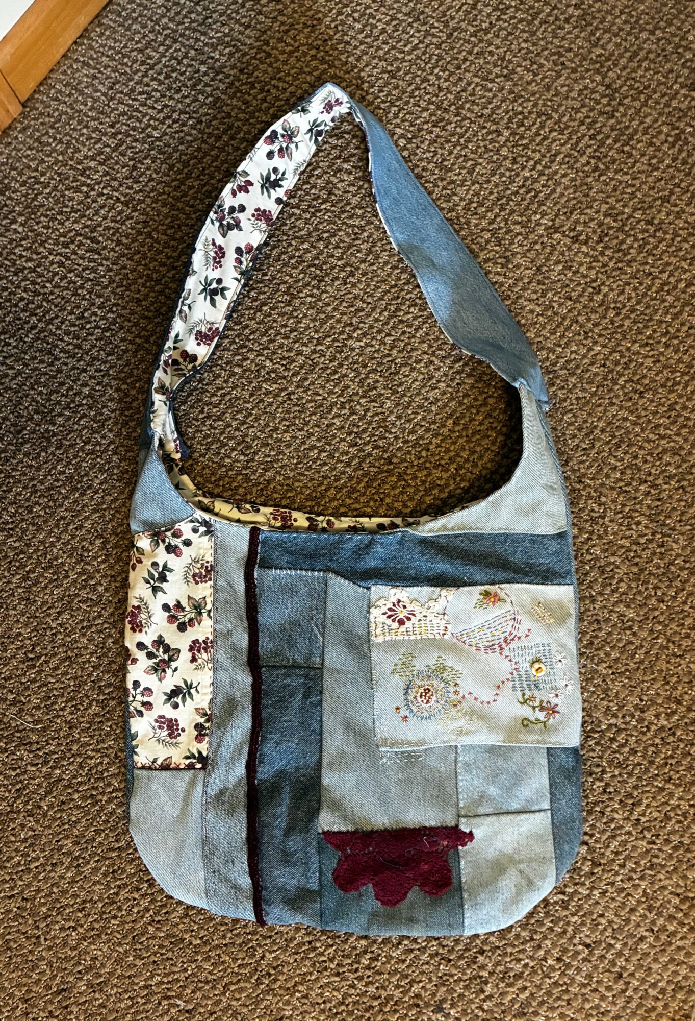 Fabric shoulder bag with floral, denim, and decorative patches on a brown textured surface.