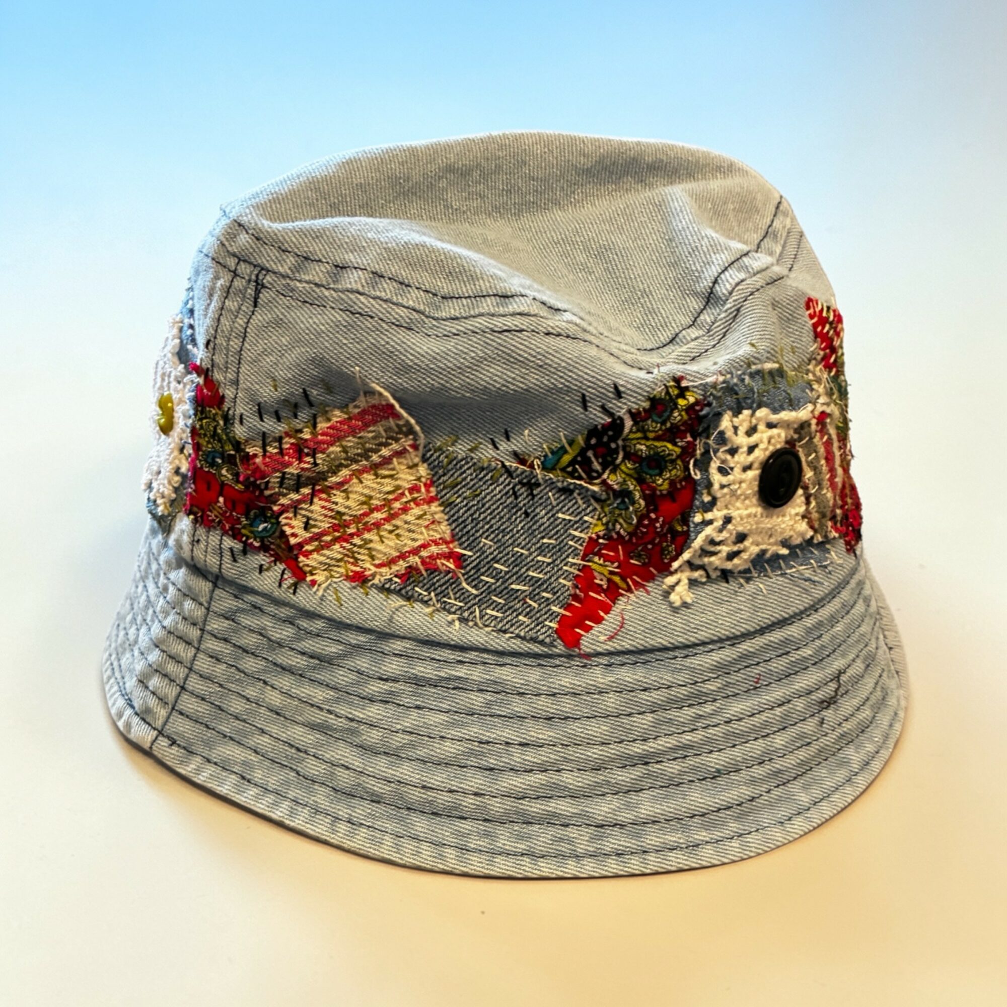 Gray bucket hat with embroidered red, yellow, and black designs, and stitched patterns, on a plain background.