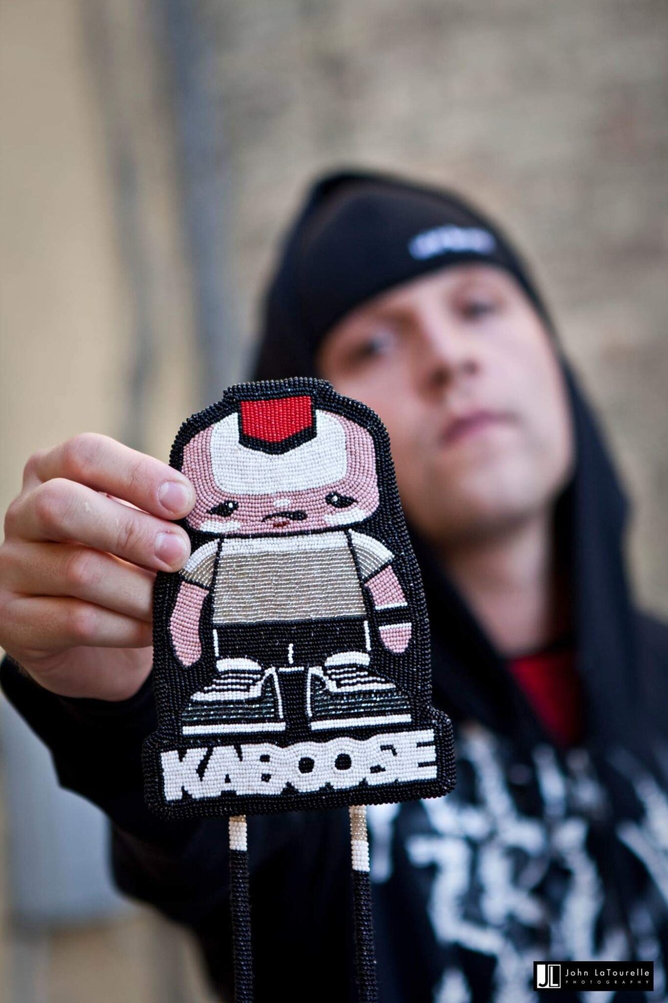 Person holding a KABOOSE patch featuring a cartoon character with a red hat, black and white clothing, and a neutral expression.