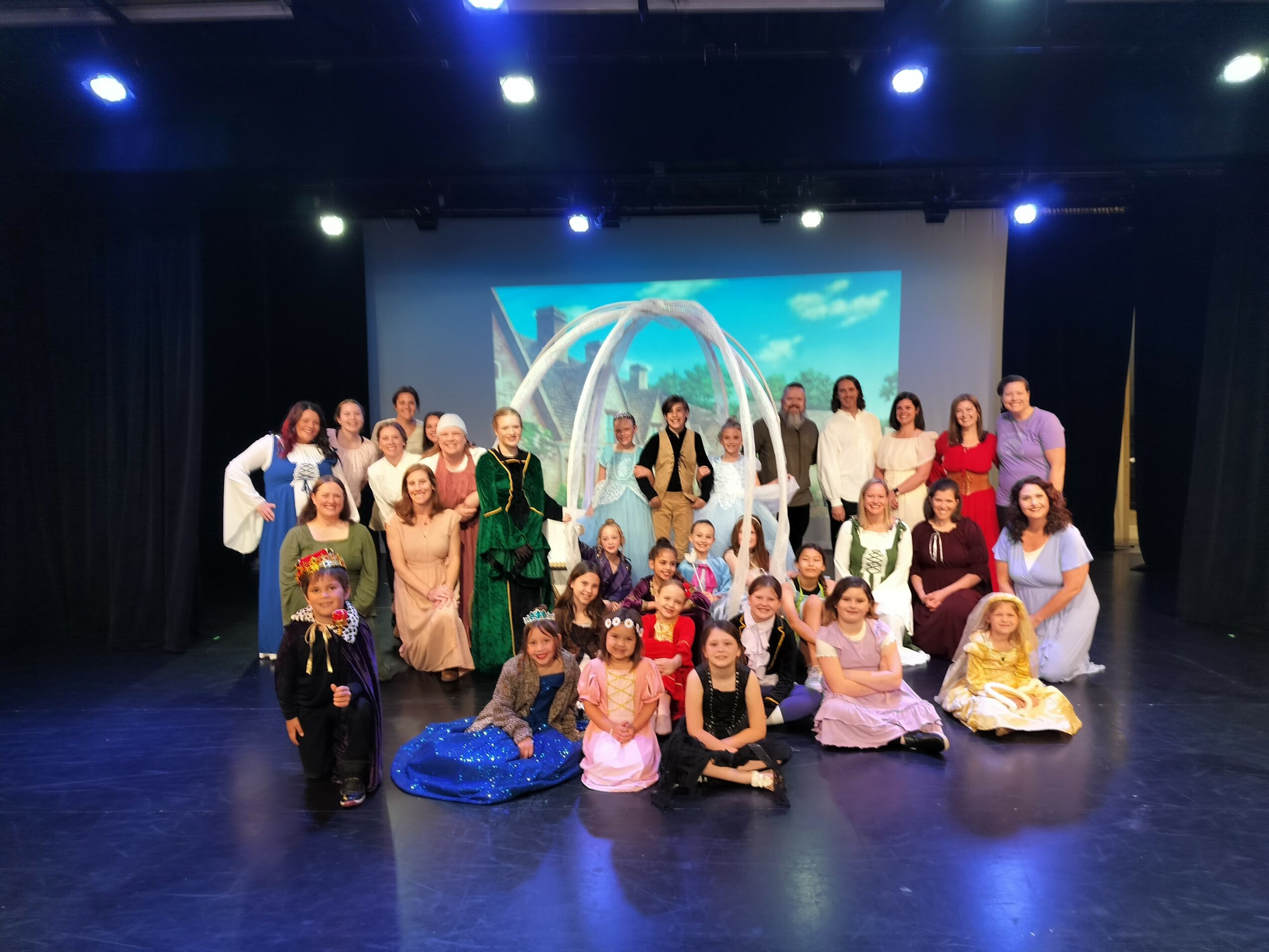 Group of people on stage with a blue and white backdrop, some in costumes, posing for a photo.