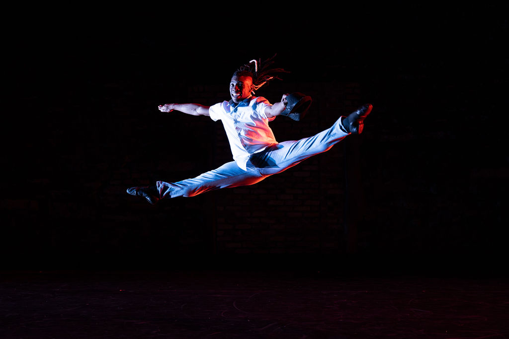 Person in white outfit performing a high jump or split leap against a dark background.