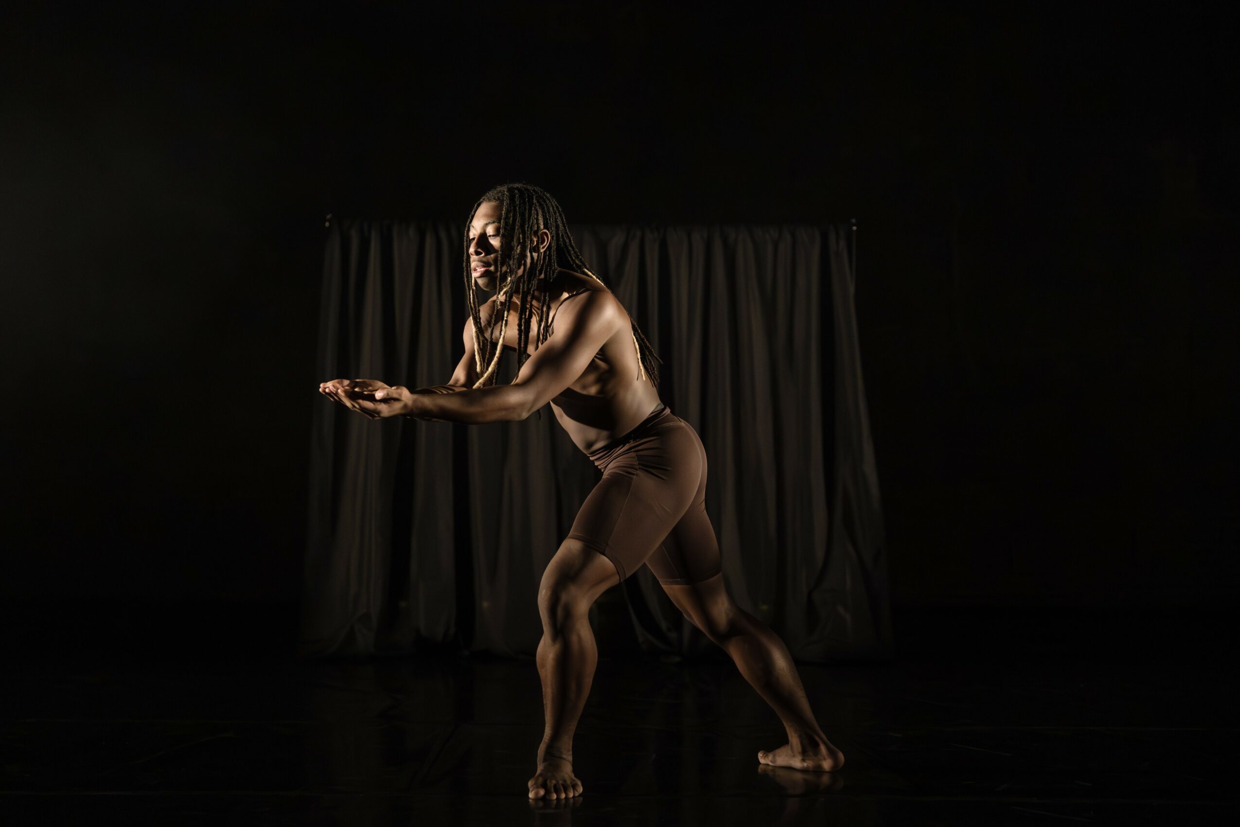 A woman with long hair in a dance pose on a dark stage with a curtain background.