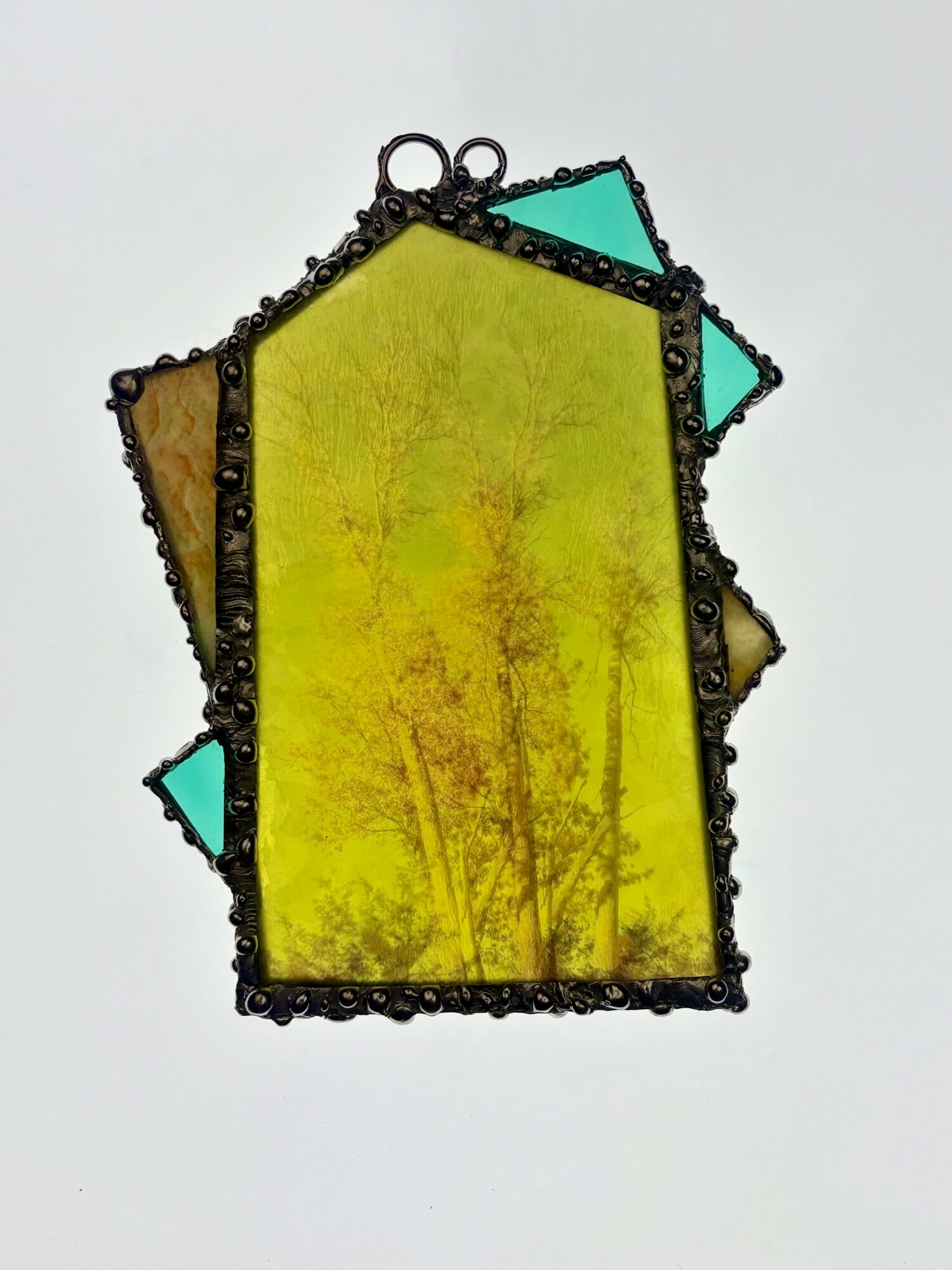 Colorful stained glass piece with yellow, green, and blue sections, outlined with black beads, on a white background.