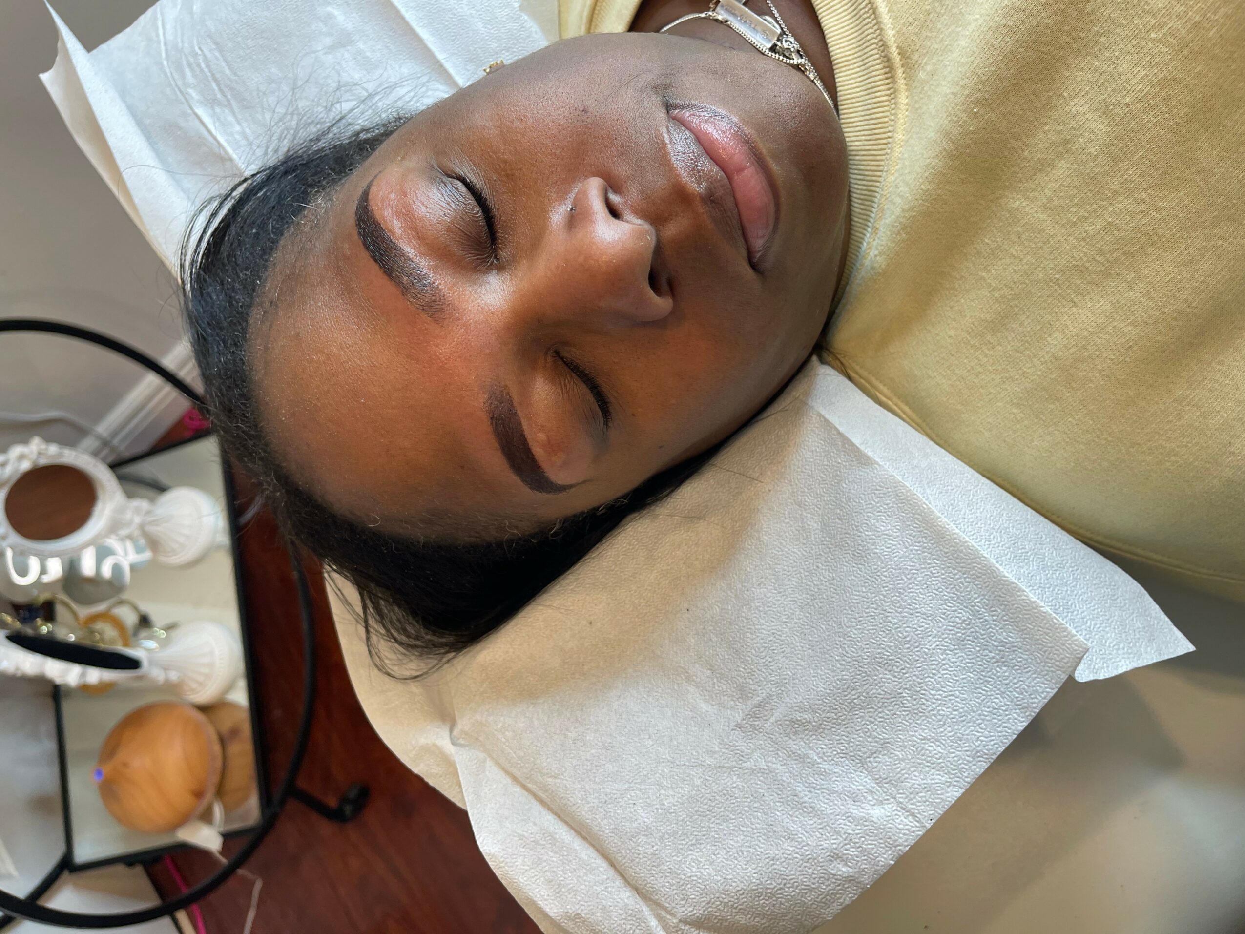 Woman lying with eyes closed on a pillow, appearing to be resting or sleeping, with skincare products nearby.