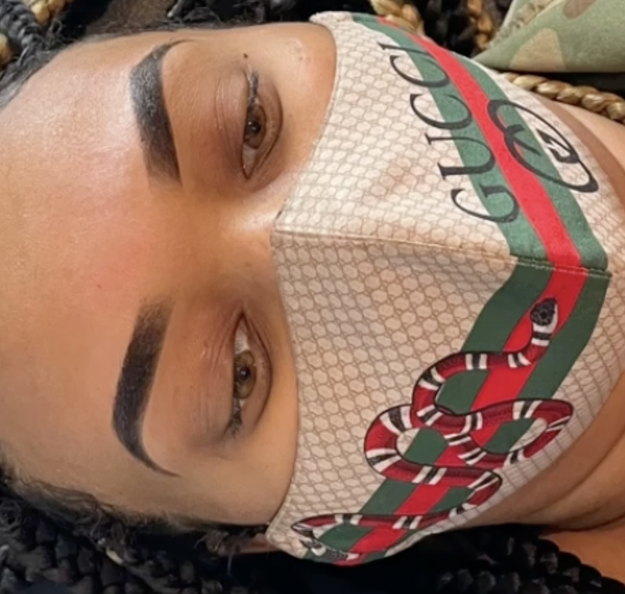 Close-up of a person's face wearing a patterned face mask with a logo, lying down with eyes open.