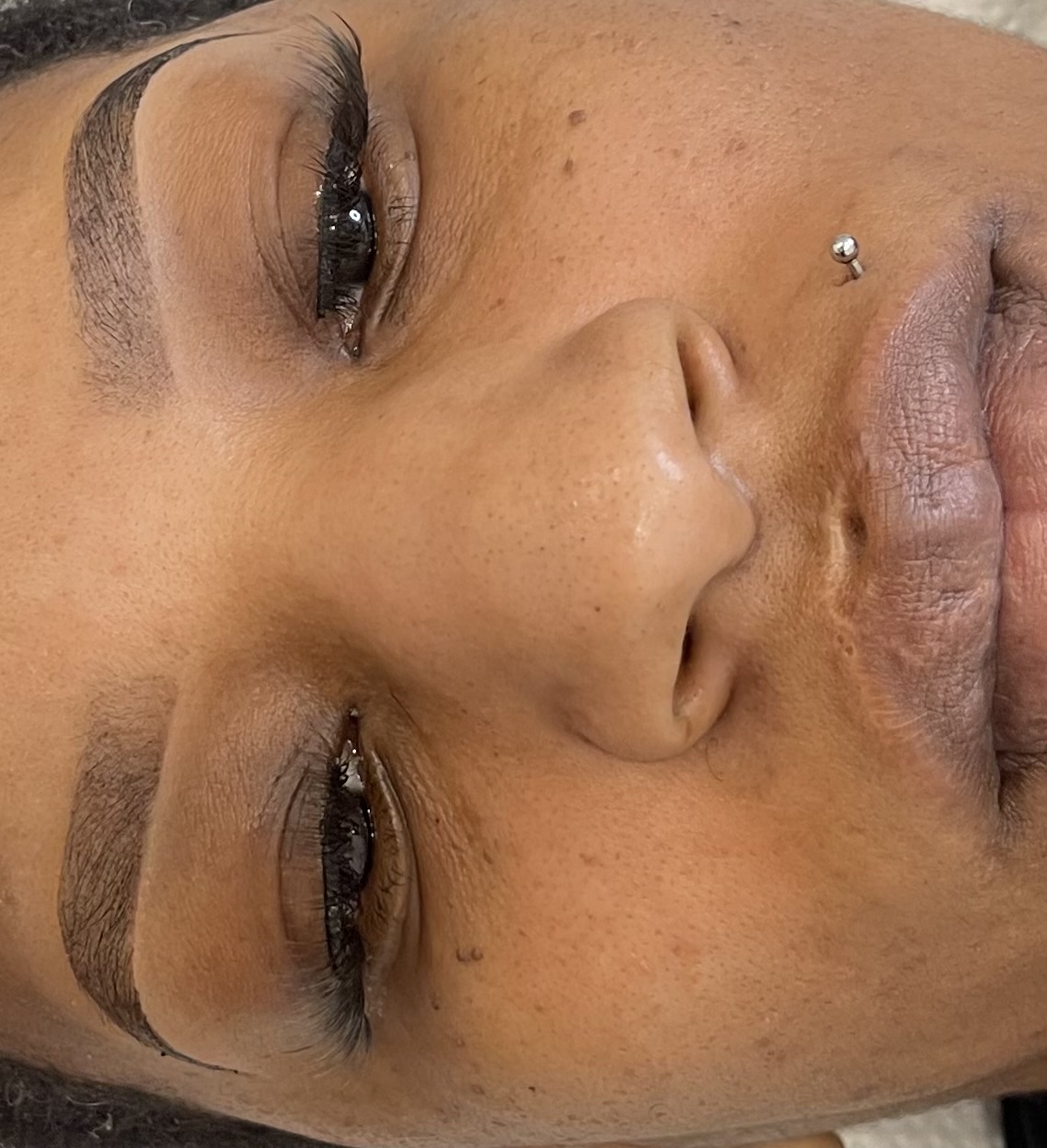 Close-up of a person's face with closed eyes, a nose piercing, and visible skin details.