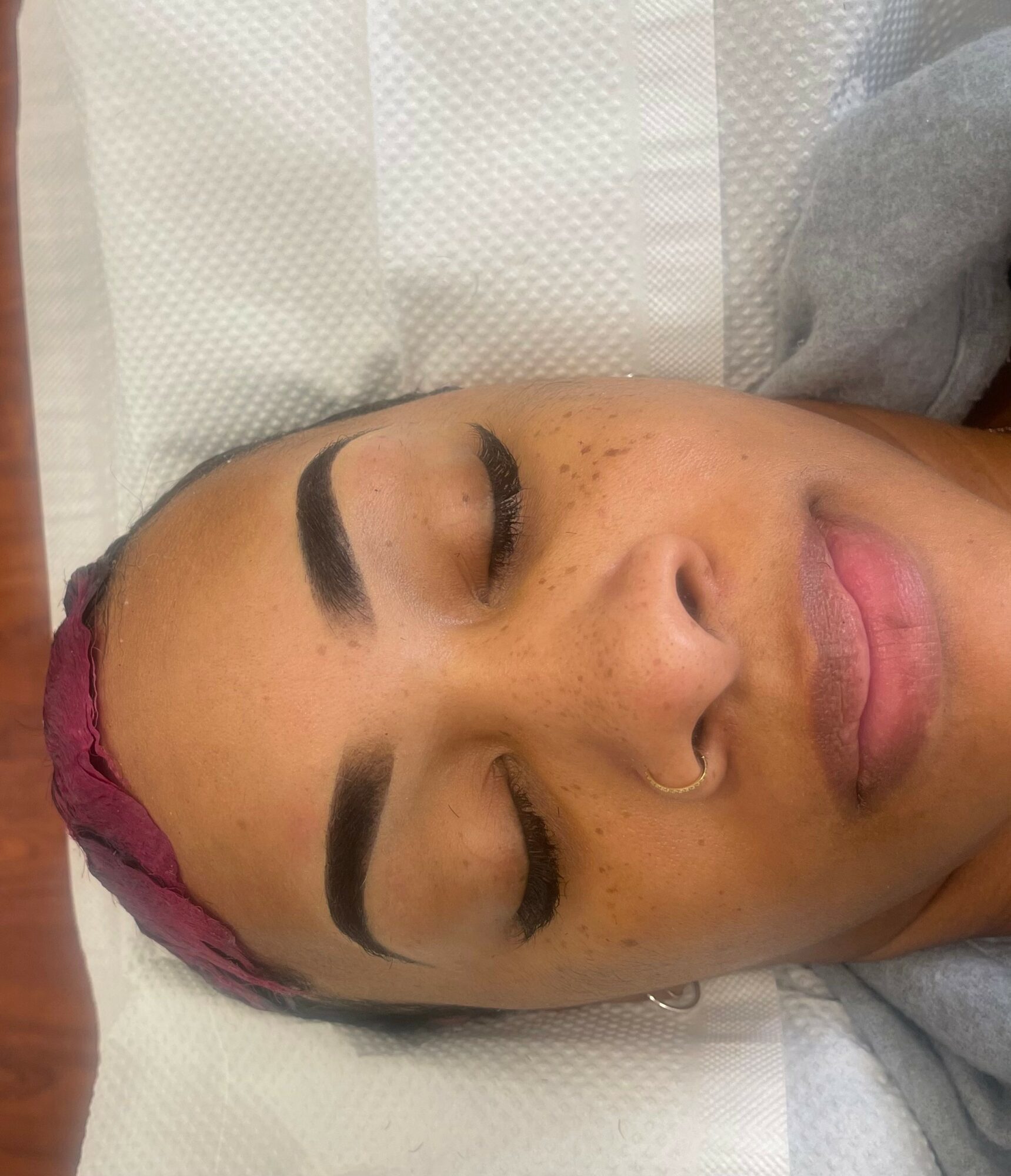 Woman with closed eyes, lying down, with makeup and a head covering, on a white surface.