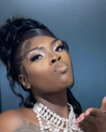 Woman with styled hair and jewelry blowing a kiss, against a blue background.