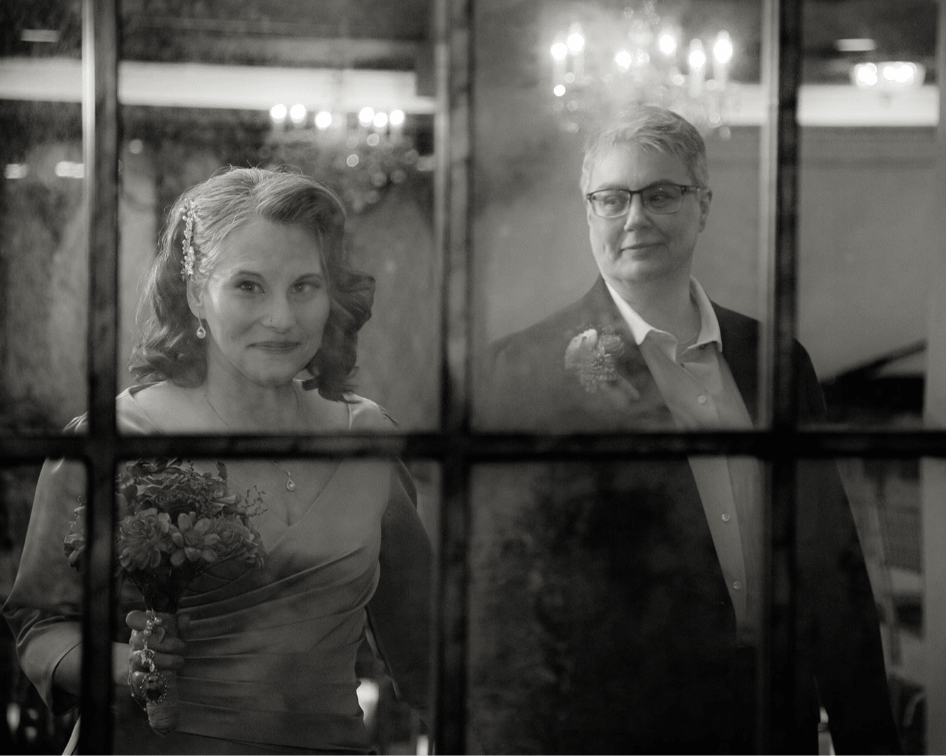 Two people, a woman and a man, seen through a window with a grid pattern, in a black and white photo.