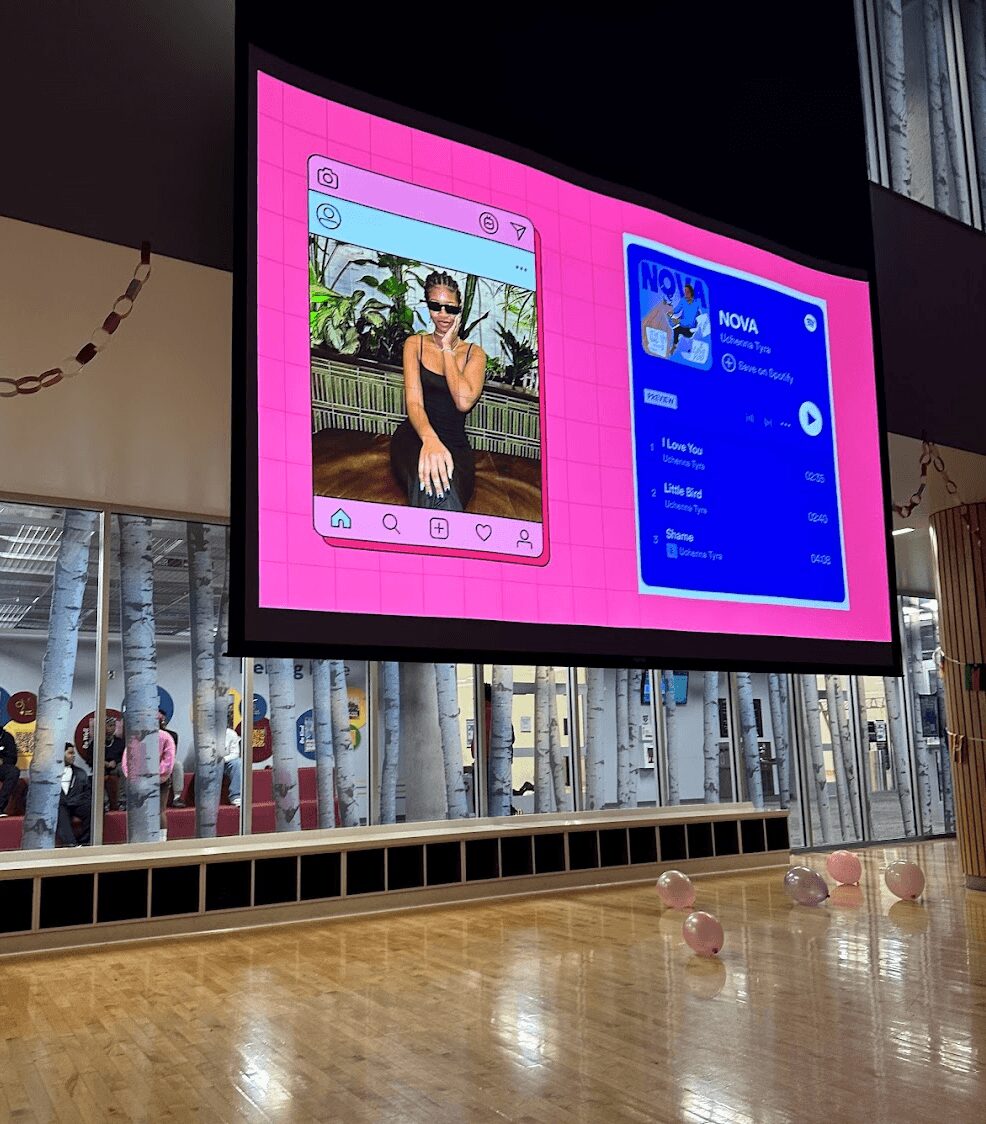 Large digital screen displaying a woman in sunglasses and a black outfit, with a pink background and social media interface, in a public space.