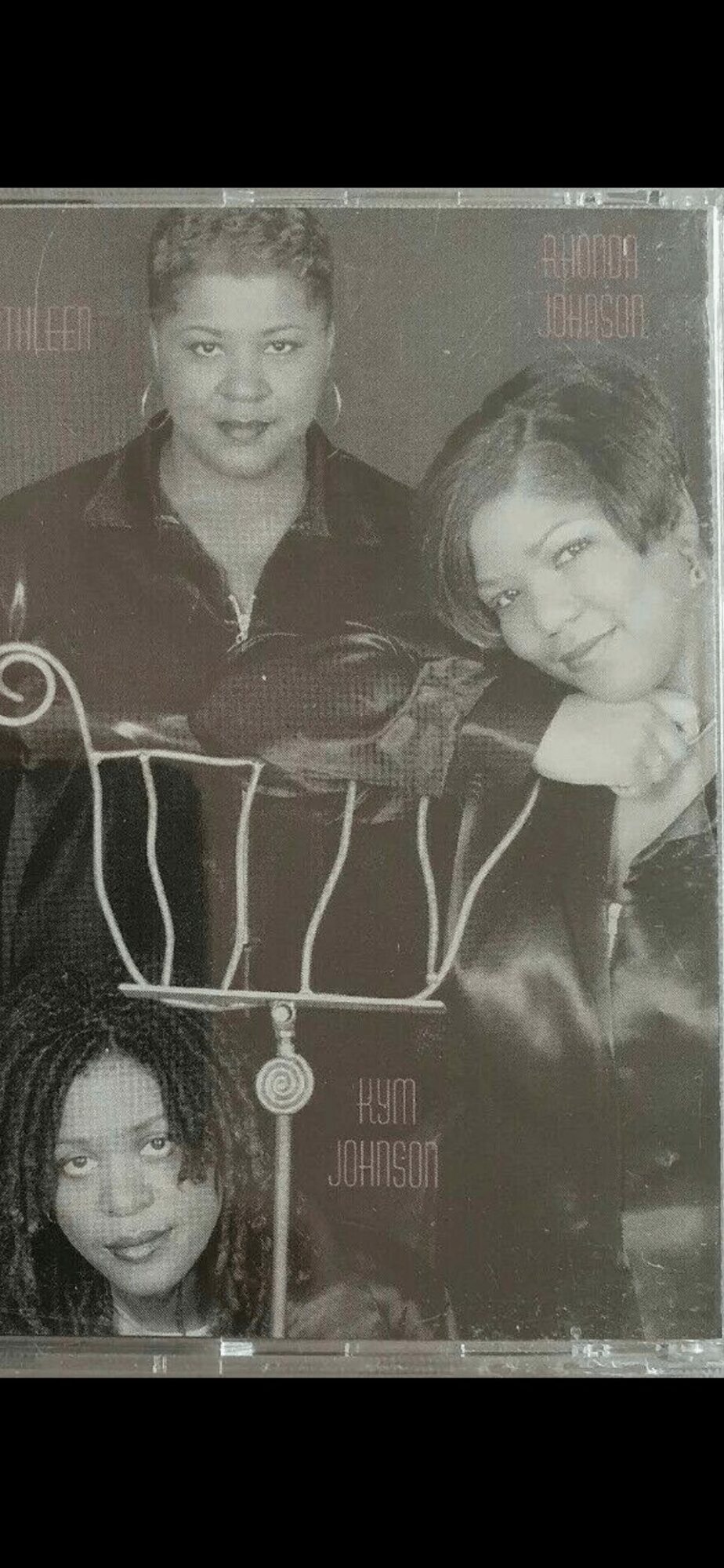 Three women pose together, two standing and one sitting, with a decorative background, in black and white.