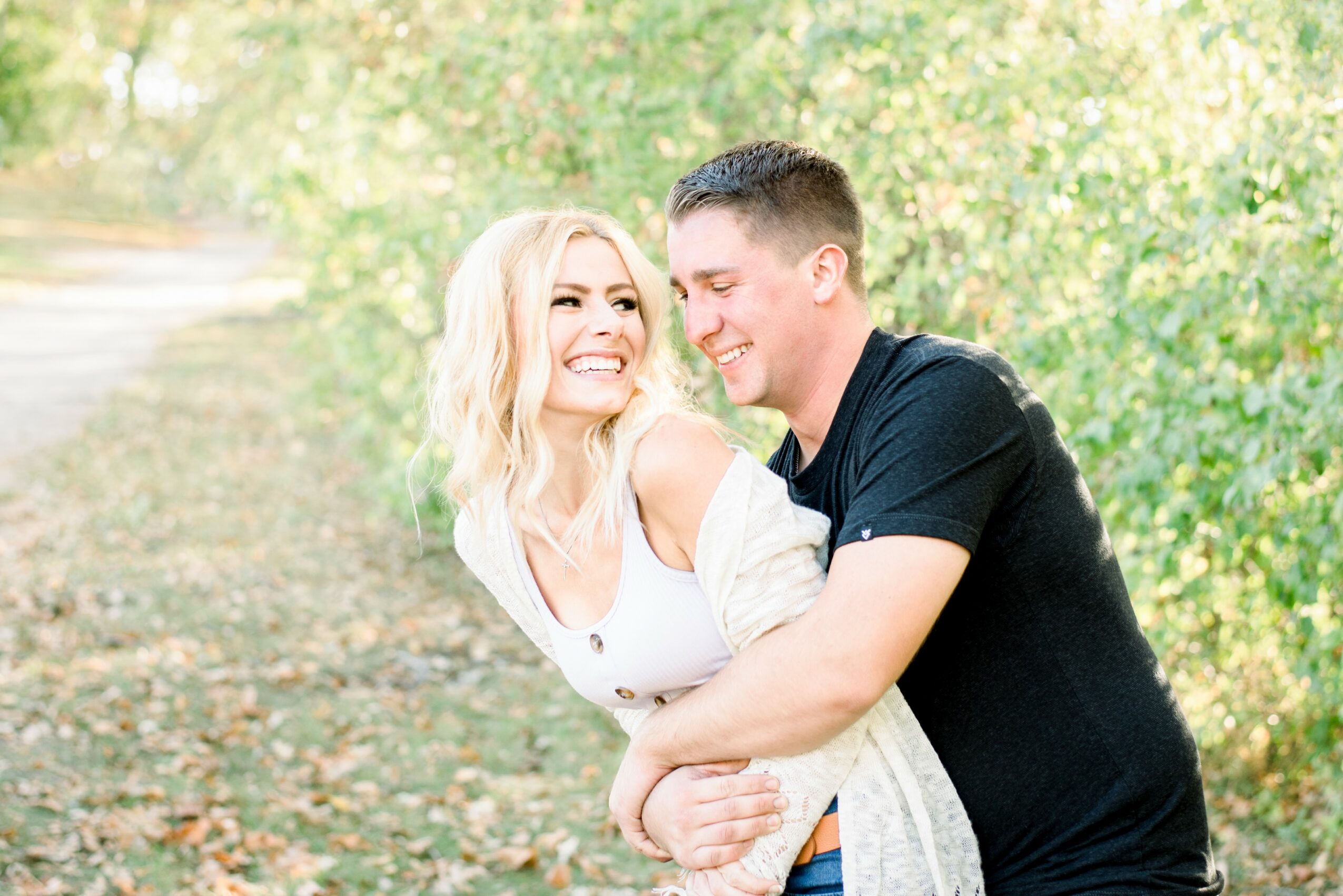 A smiling couple embracing outdoors with green trees in the background.