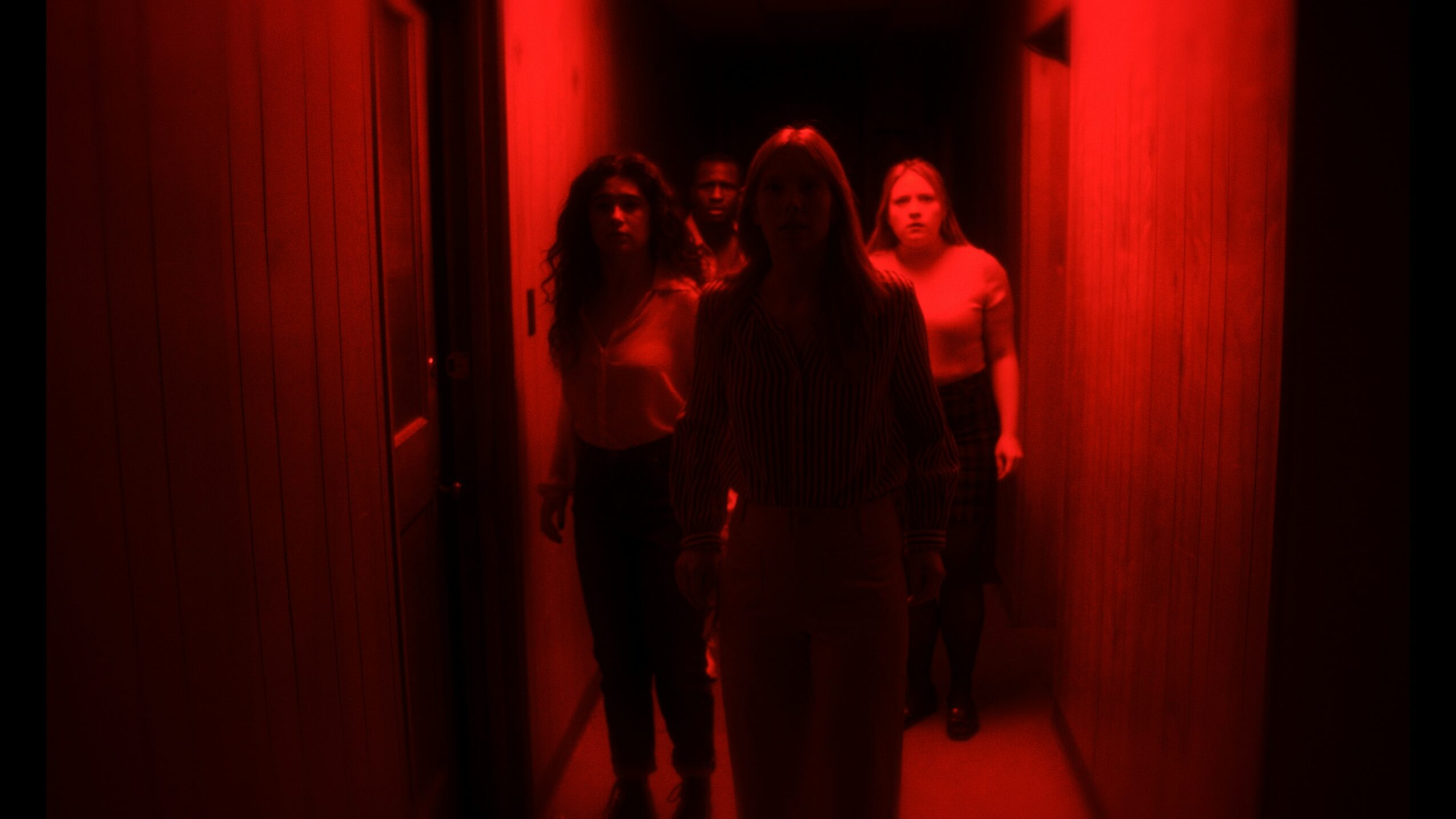 Three people walking down a dimly lit corridor with red lighting, shadows obscuring their faces.