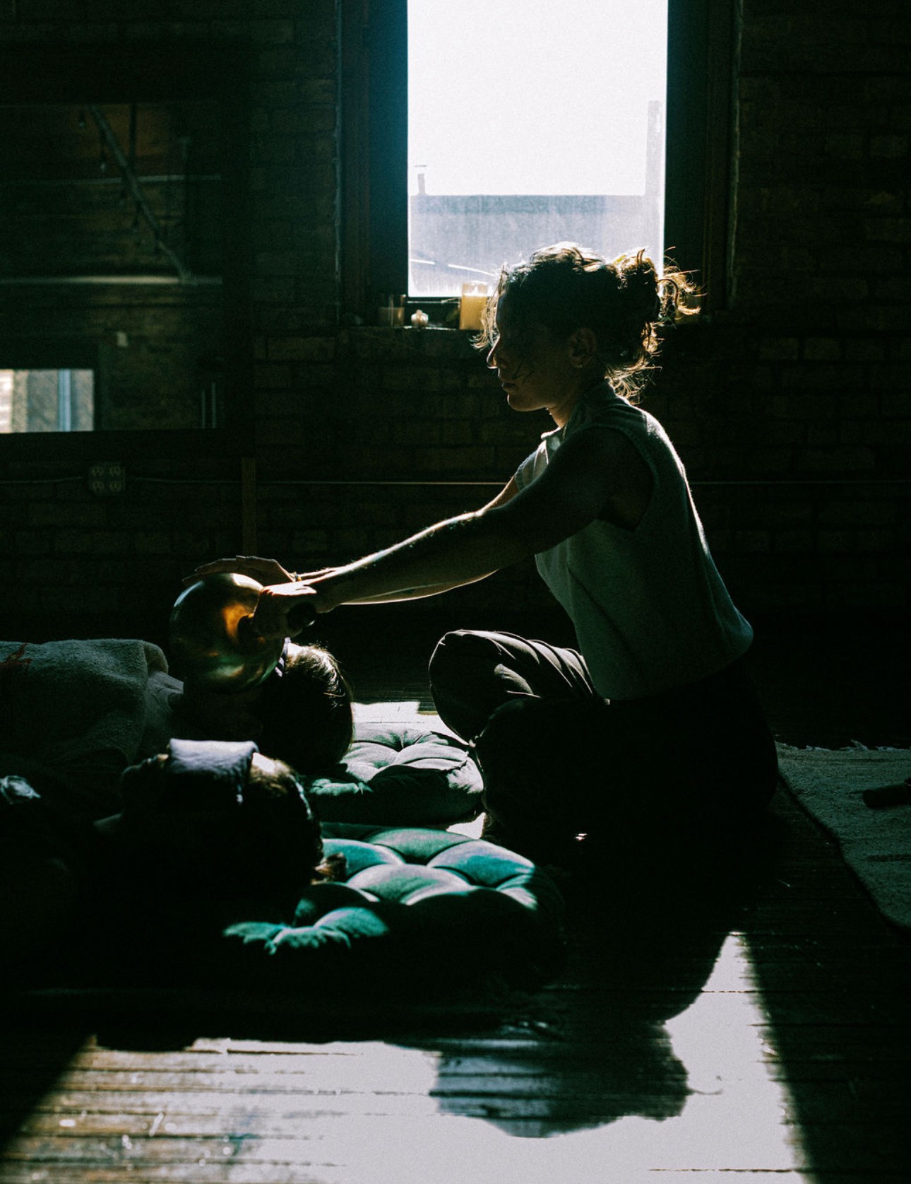 Child sitting on the floor near a window, reaching out to a doll, with sunlight streaming in. Word count: 20.