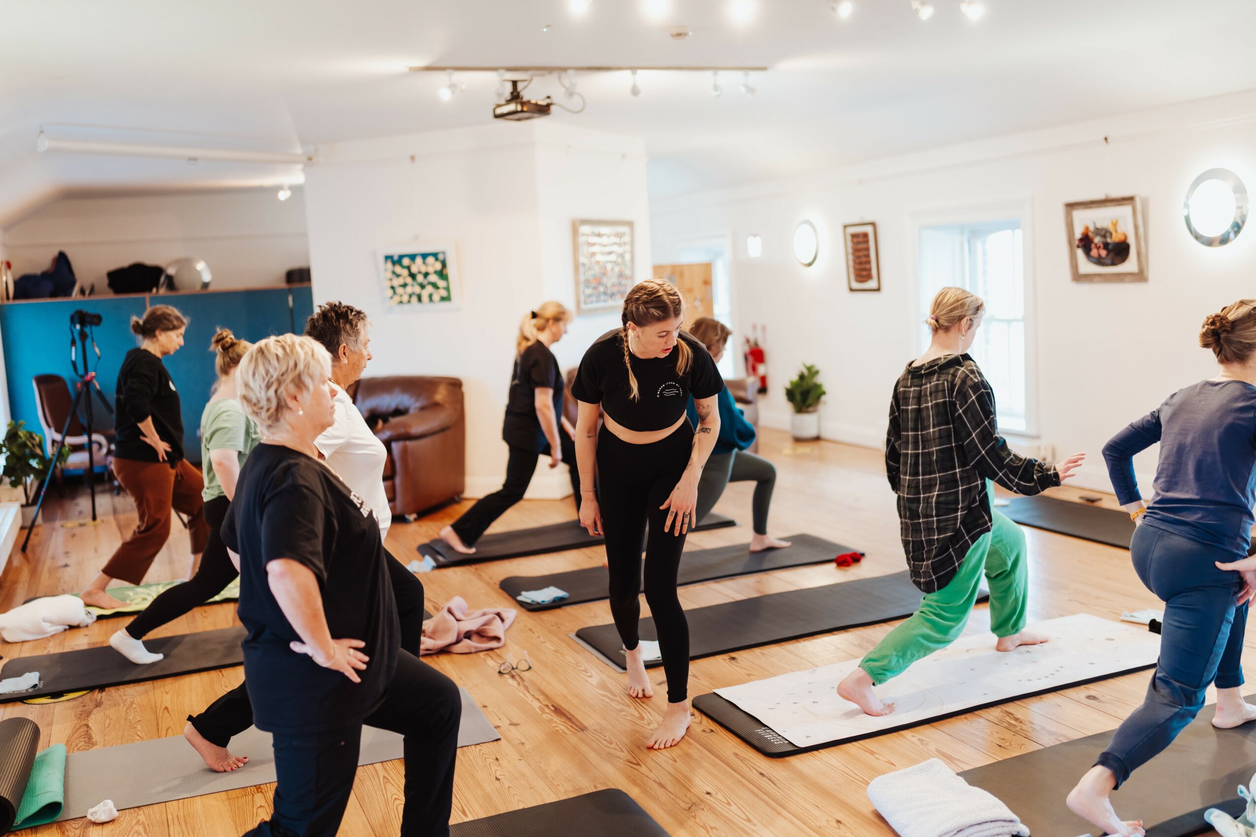 Group of people participating in a yoga or exercise class in a bright, spacious room with mats on the floor.