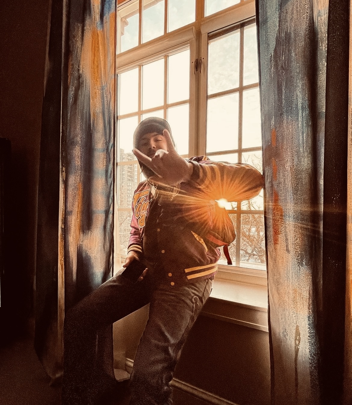 Person sitting by a window with sunlight shining through, surrounded by curtains, indoors.