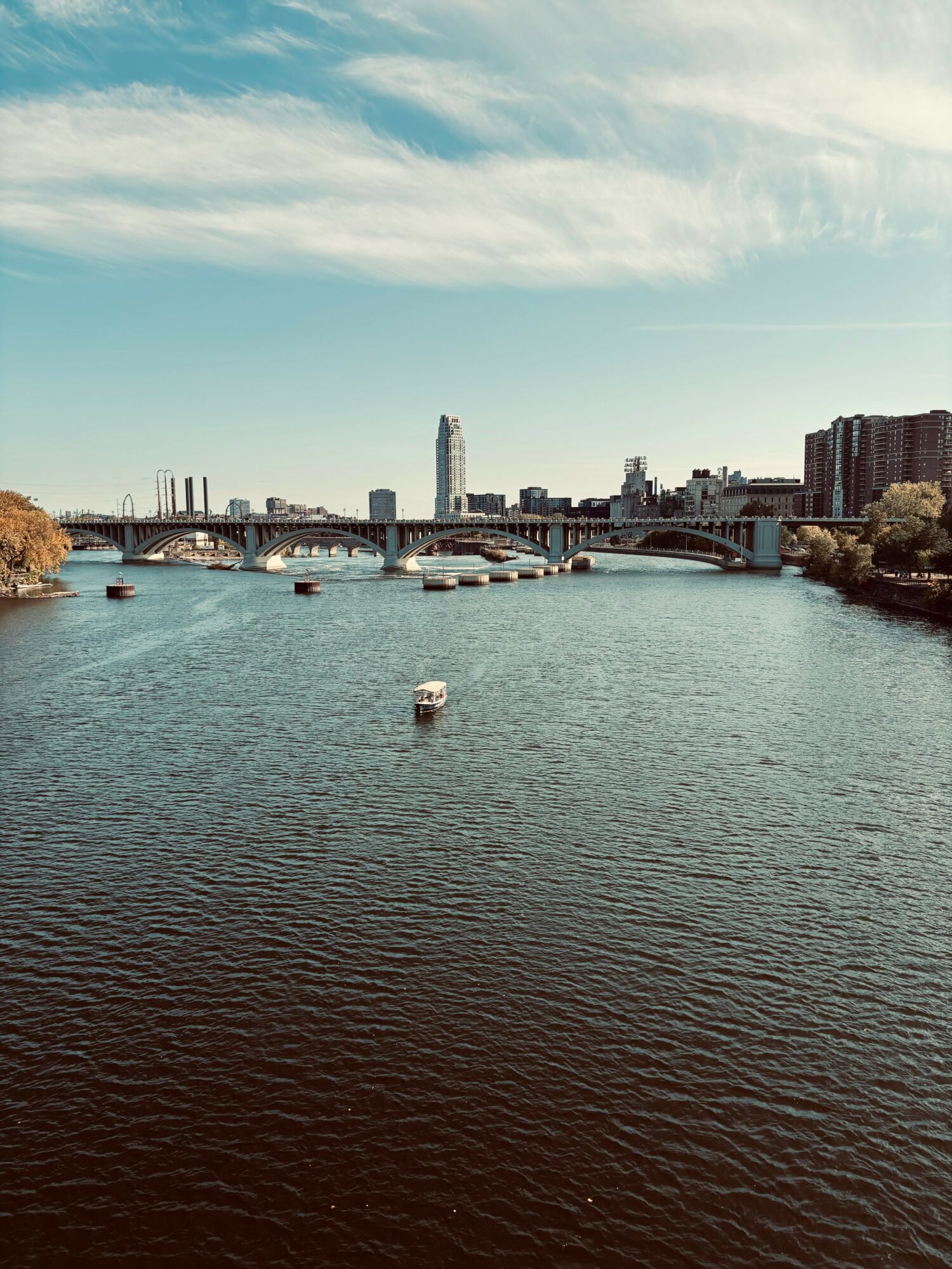 River with boats, bridge, city skyline, and partly cloudy sky, viewed from a low angle.