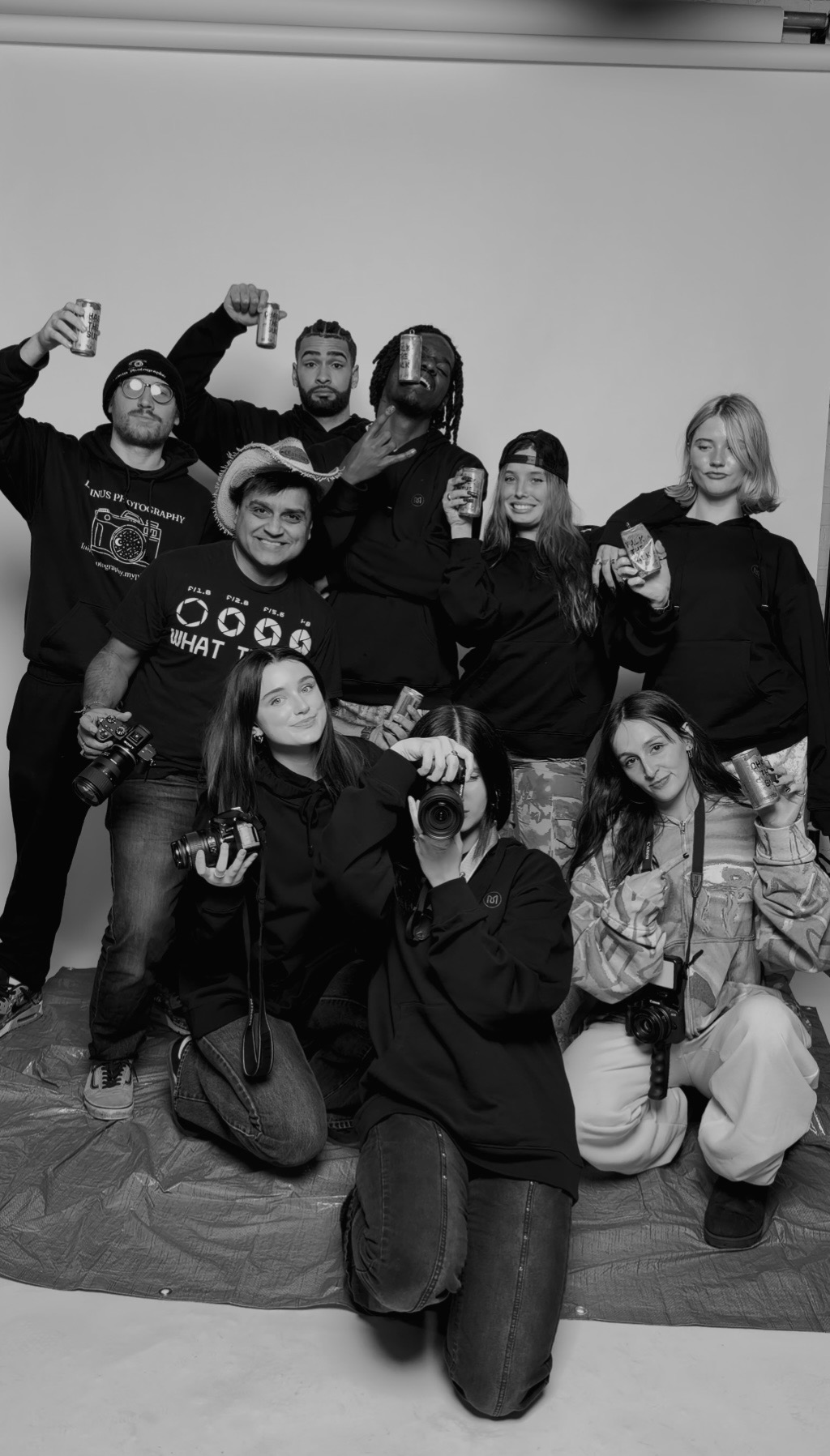 Group of nine people posing together, some holding drinks, in a room with a plain background.
