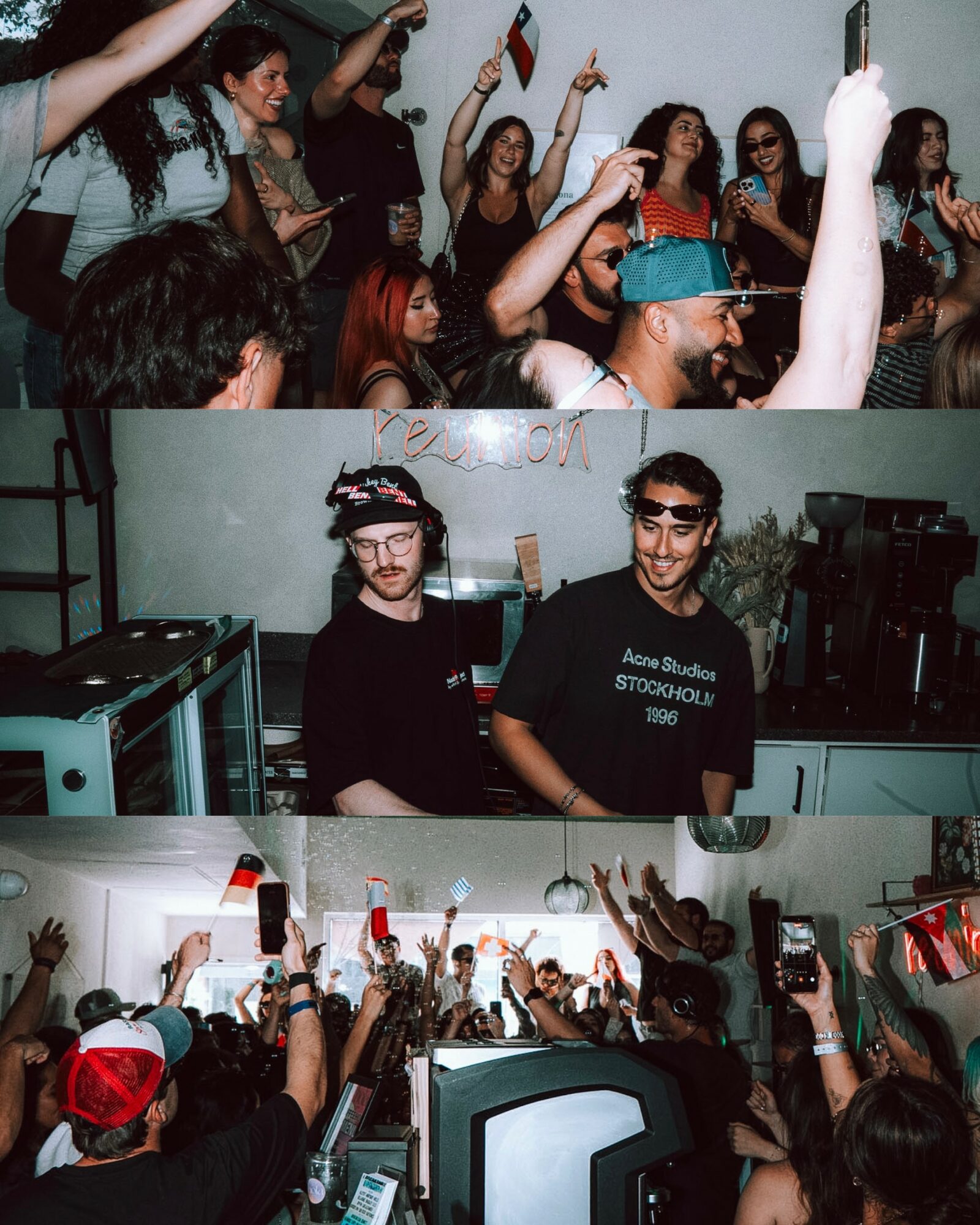 Crowd of people at a party, some holding drinks and phones, with two men in front wearing glasses, one with a hat, in a DJ booth.