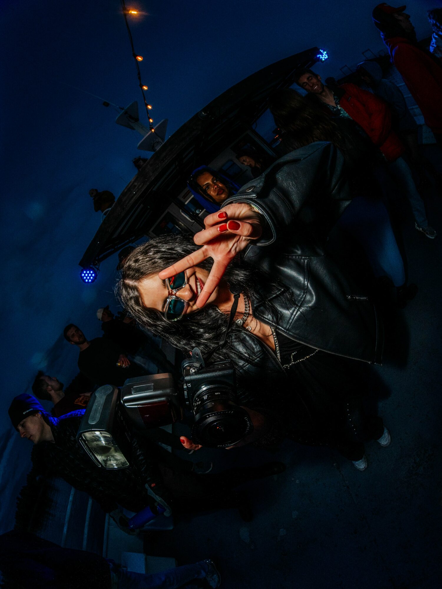 Person taking a photo with a phone at night, surrounded by people and a vehicle, in a dark outdoor setting.