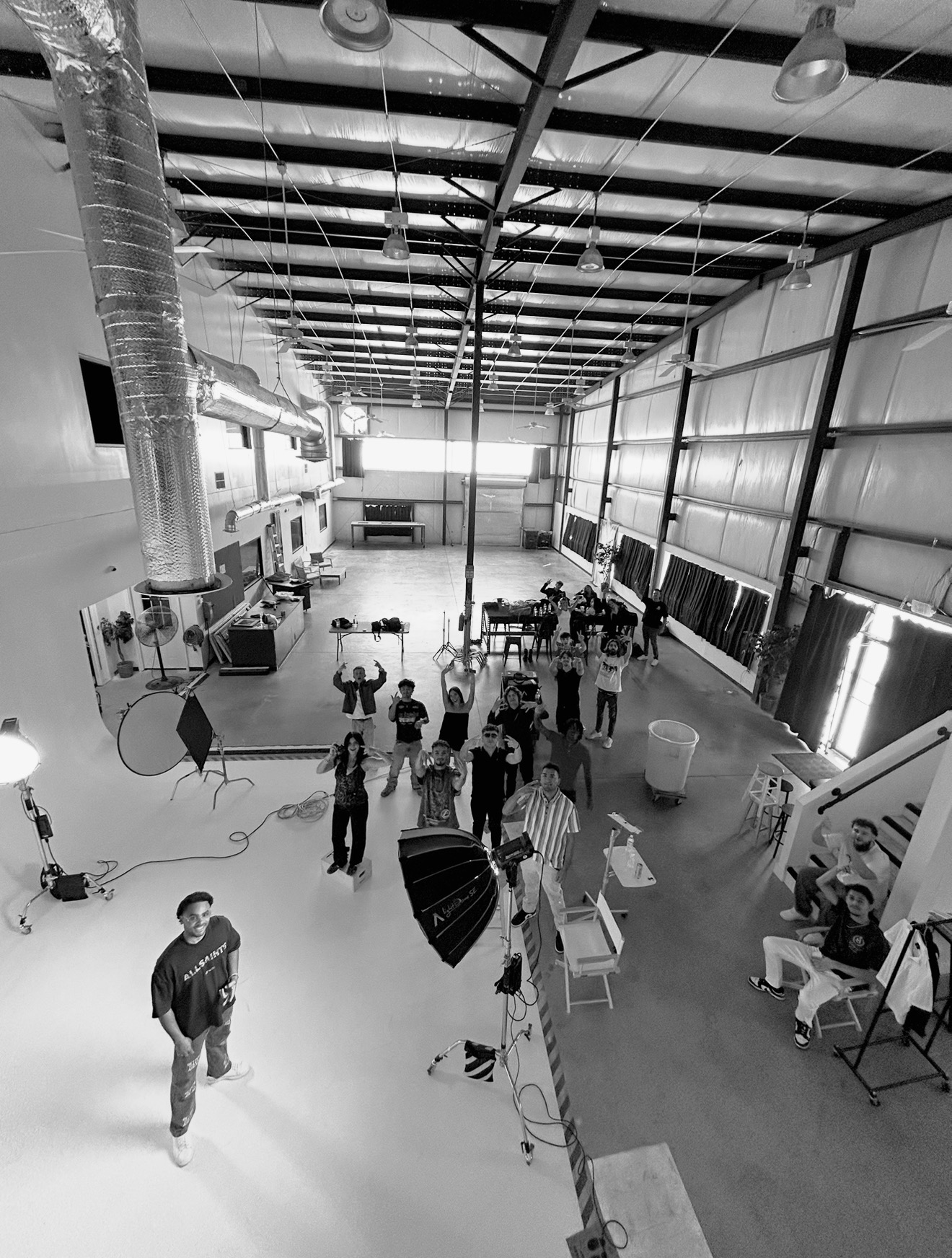 People gather inside a large industrial space with high ceilings, large ventilation ducts, and equipment, some seated at tables and others standing.