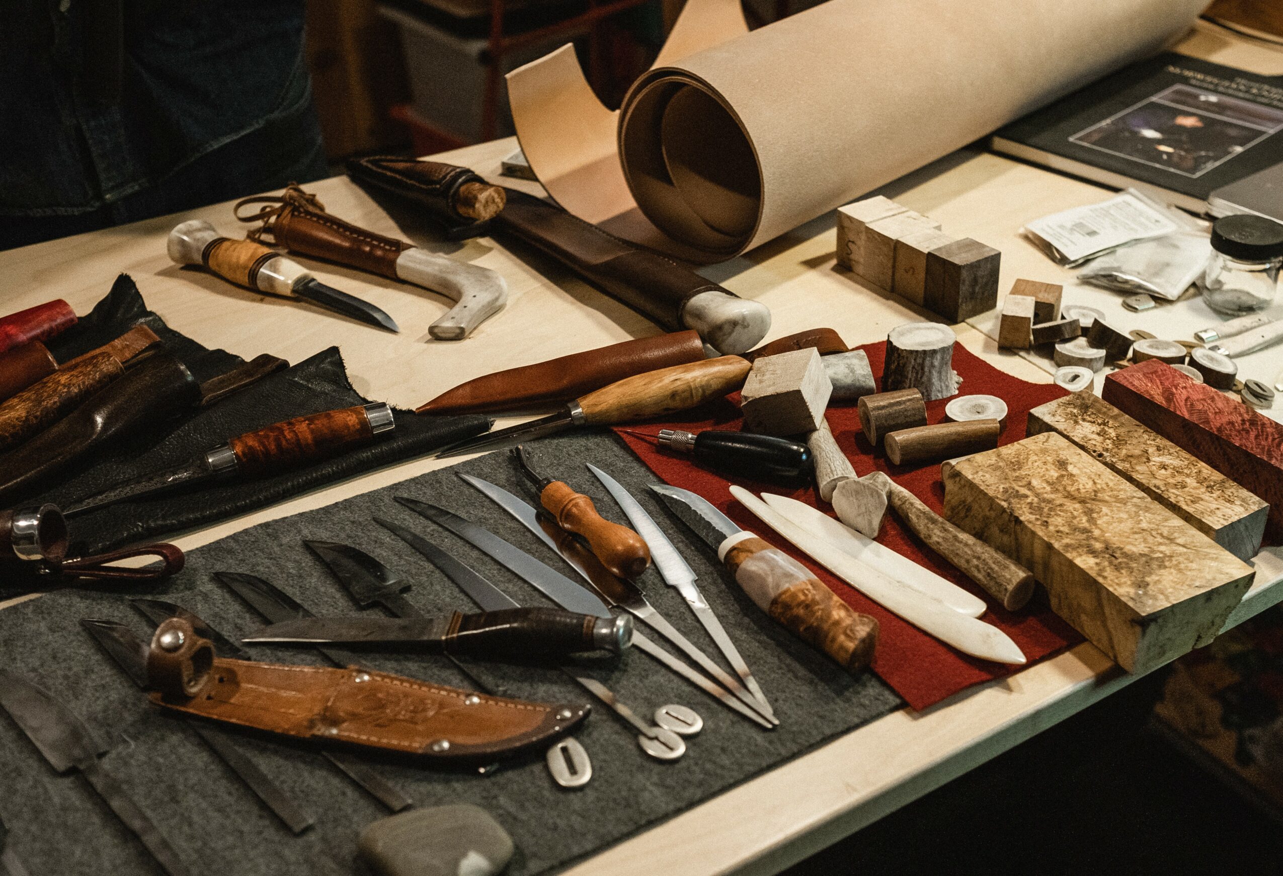 Tools and materials for bookbinding or restoration, including brushes, knives, blocks, and paper on a table.