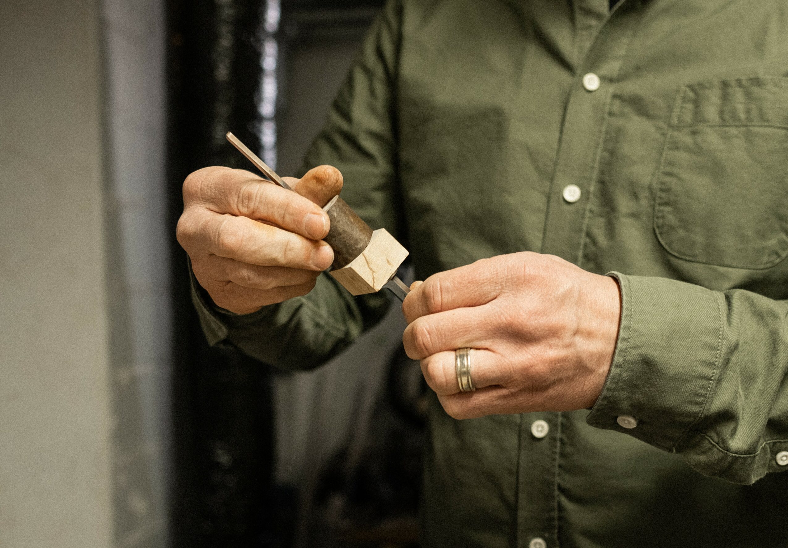 Person in green shirt holding a small object and a tool, with a ring on their finger.
