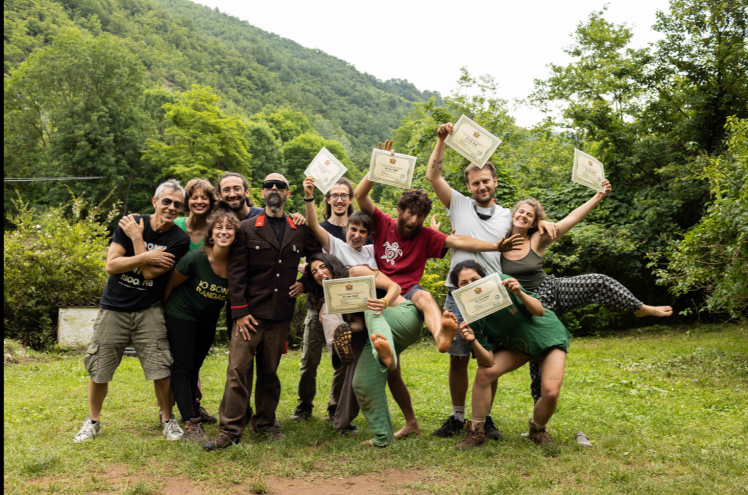 Group of people outdoors holding certificates, smiling, with trees and hills in the background.