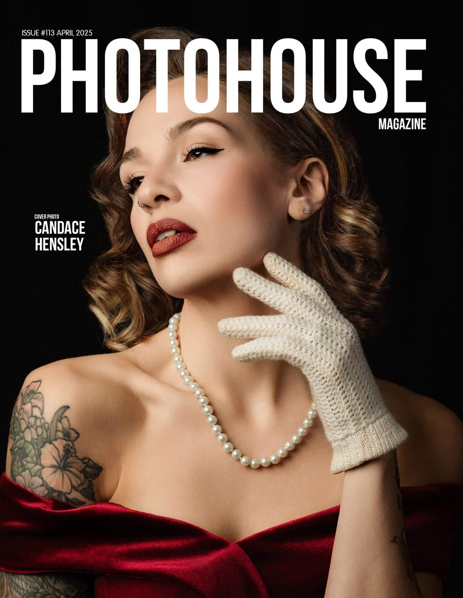 Woman with vintage style, pearl necklace, white glove, and floral tattoo, posing against black background.