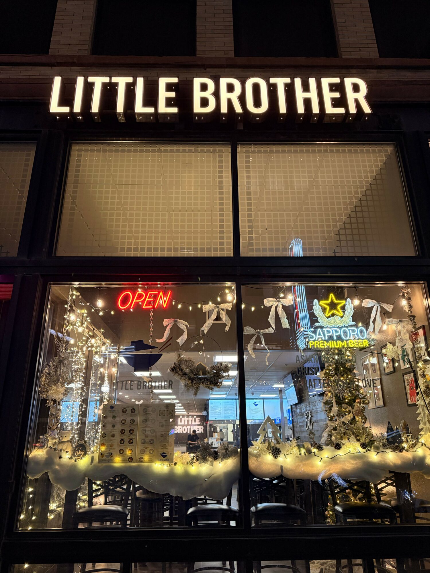 Store window with Christmas decorations, illuminated 'OPEN' sign, and a lit star, with 'LITTLE BROTHER' sign outside.