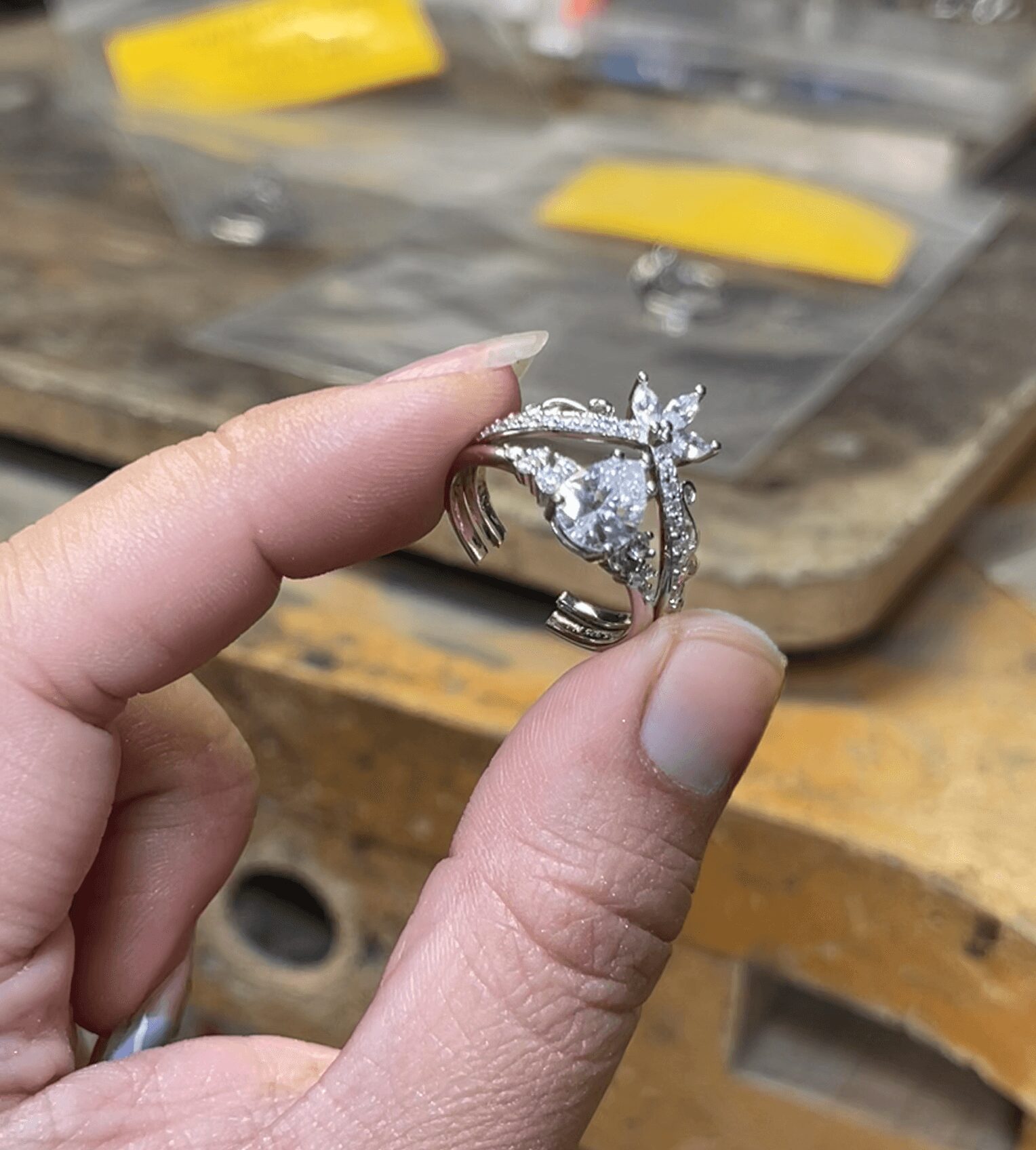 Person holding a silver ring with a large central gemstone and smaller surrounding stones, background shows jewelry display case.